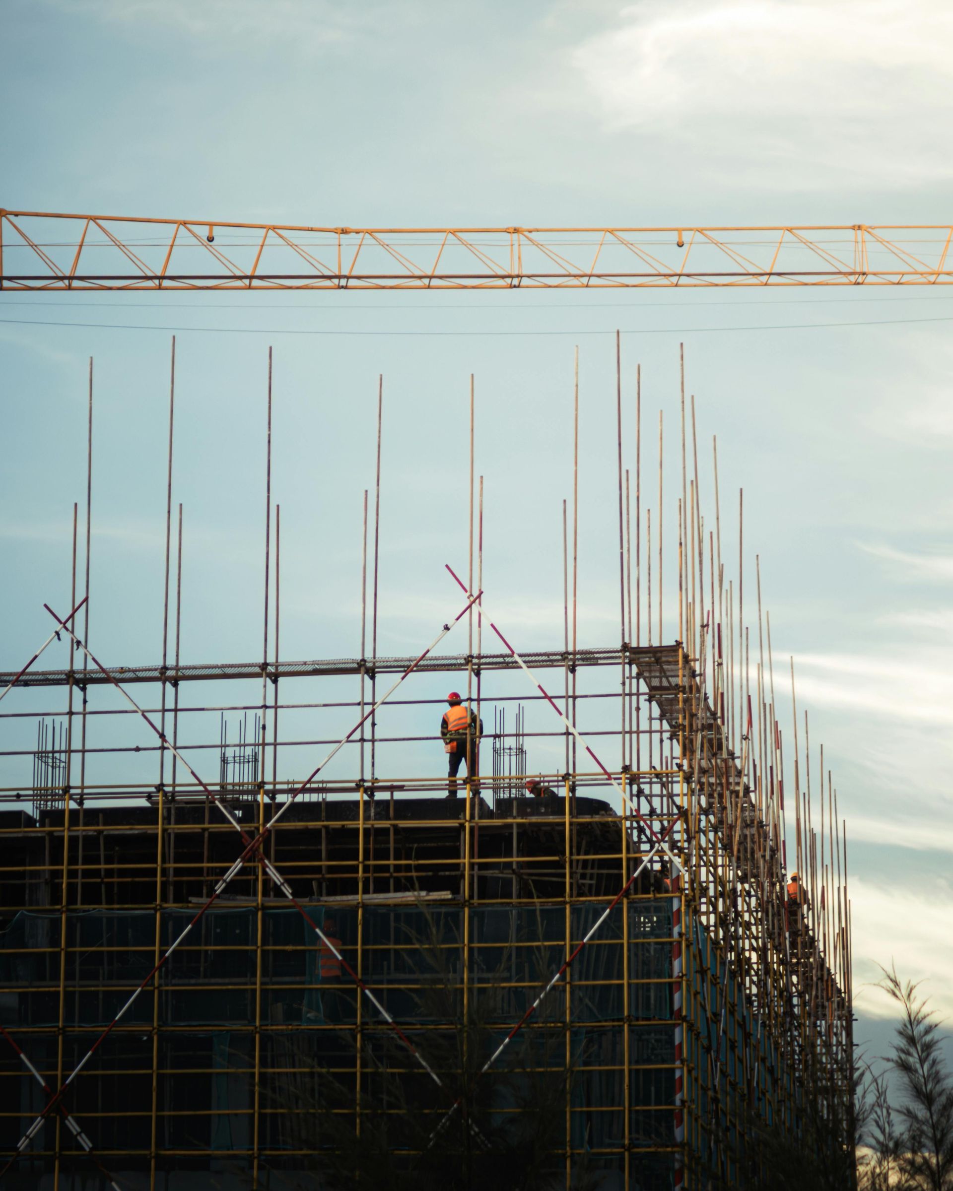 Construction site with scaffolding, a worker in a hard hat, and cranes against the sky