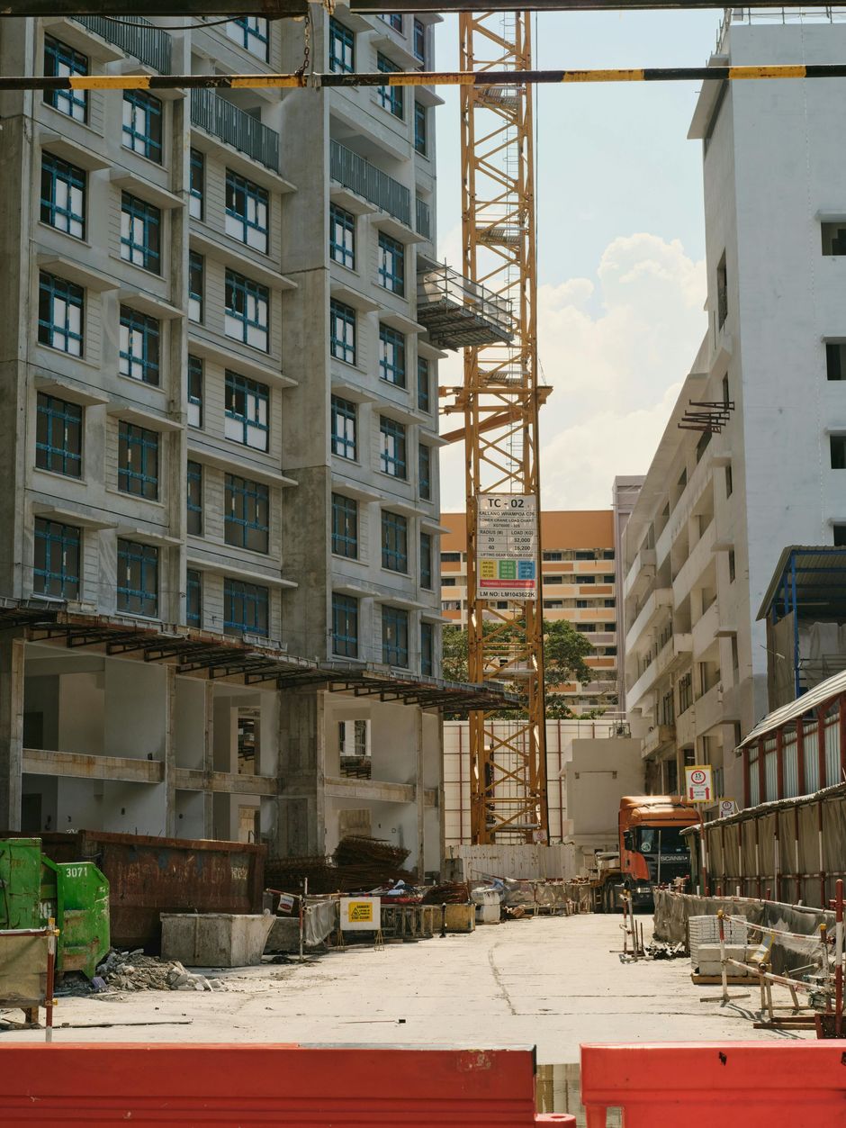 Narrow construction site between tall buildings, with a crane and unfinished concrete structures.