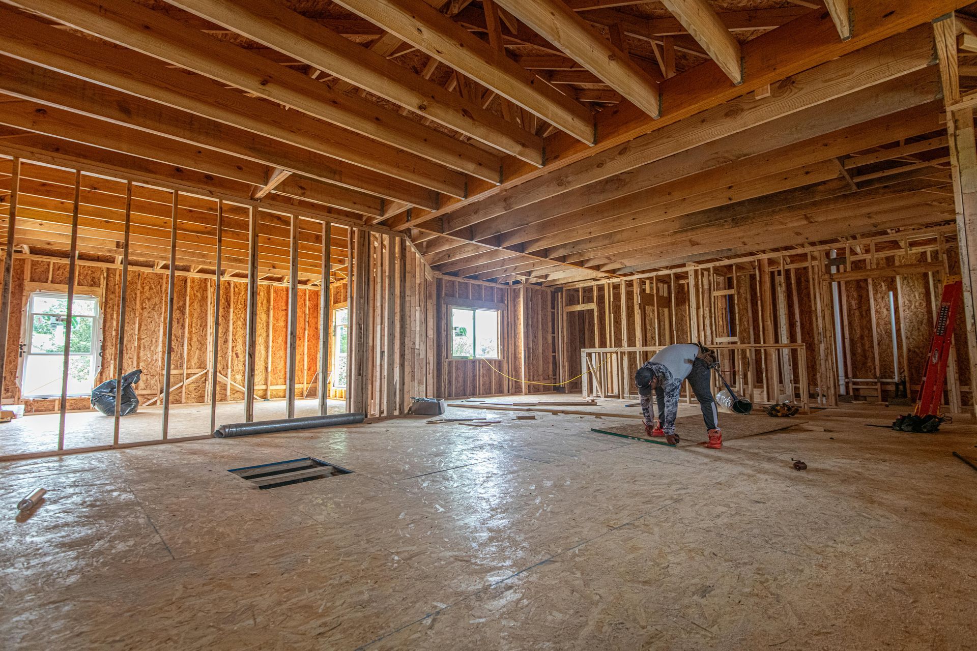 Unfinished room with exposed wood framing, and a worker bending over the floor.