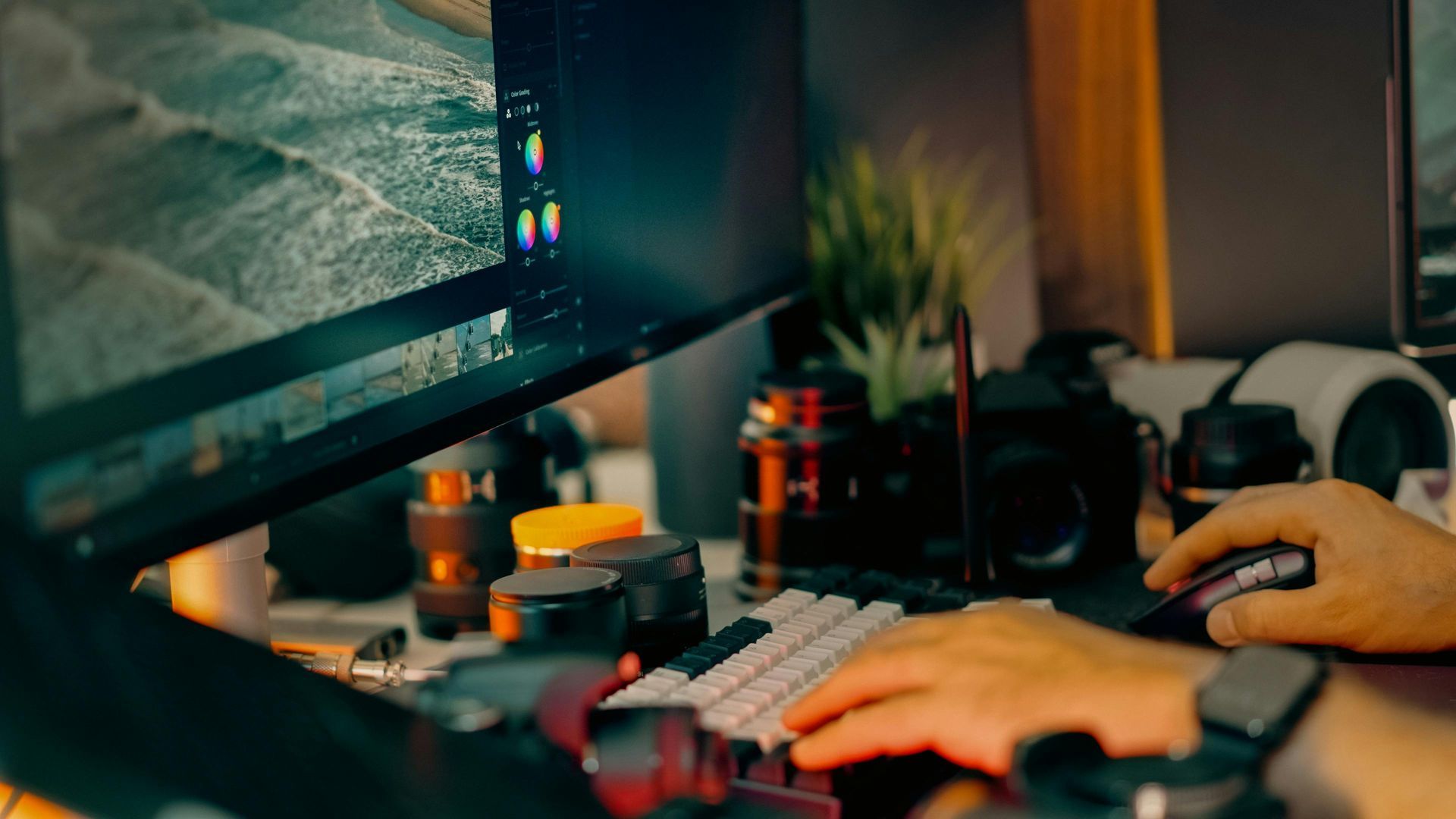 Person typing at a desk with a monitor, keyboard, mouse, and warm ambient lighting.