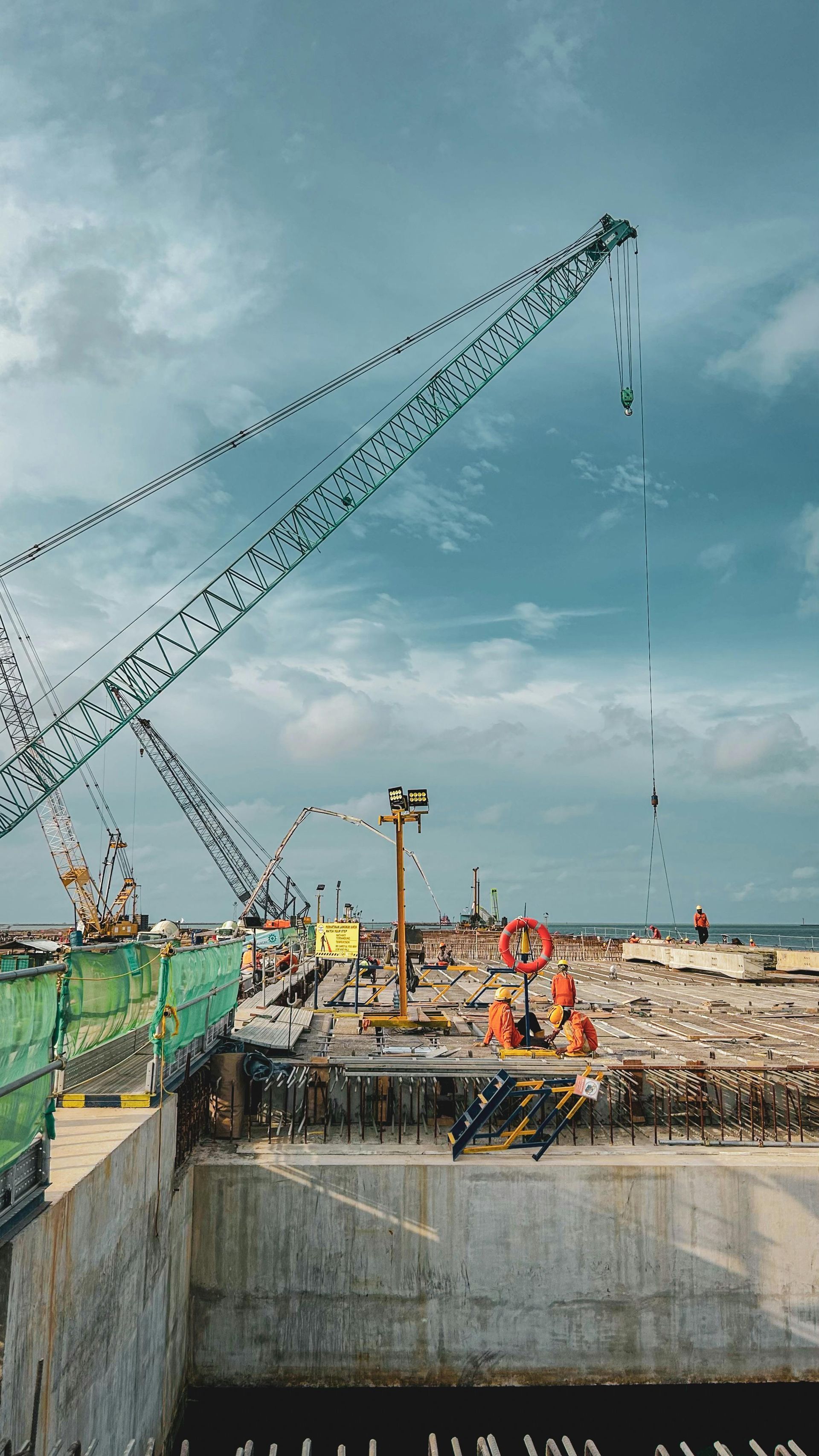 Construction site with a large crane, workers, and concrete foundation under a cloudy sky