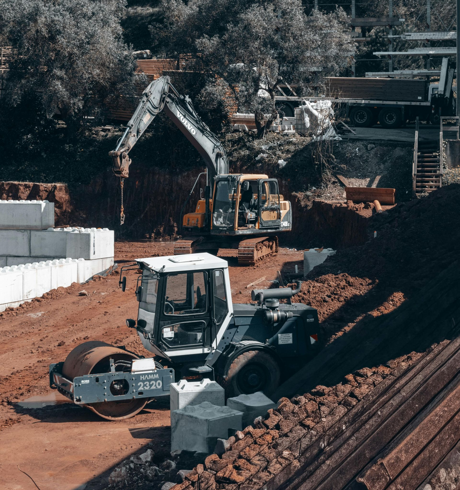 Construction site with excavators, bulldozer, and dirt piles beside a rail line.