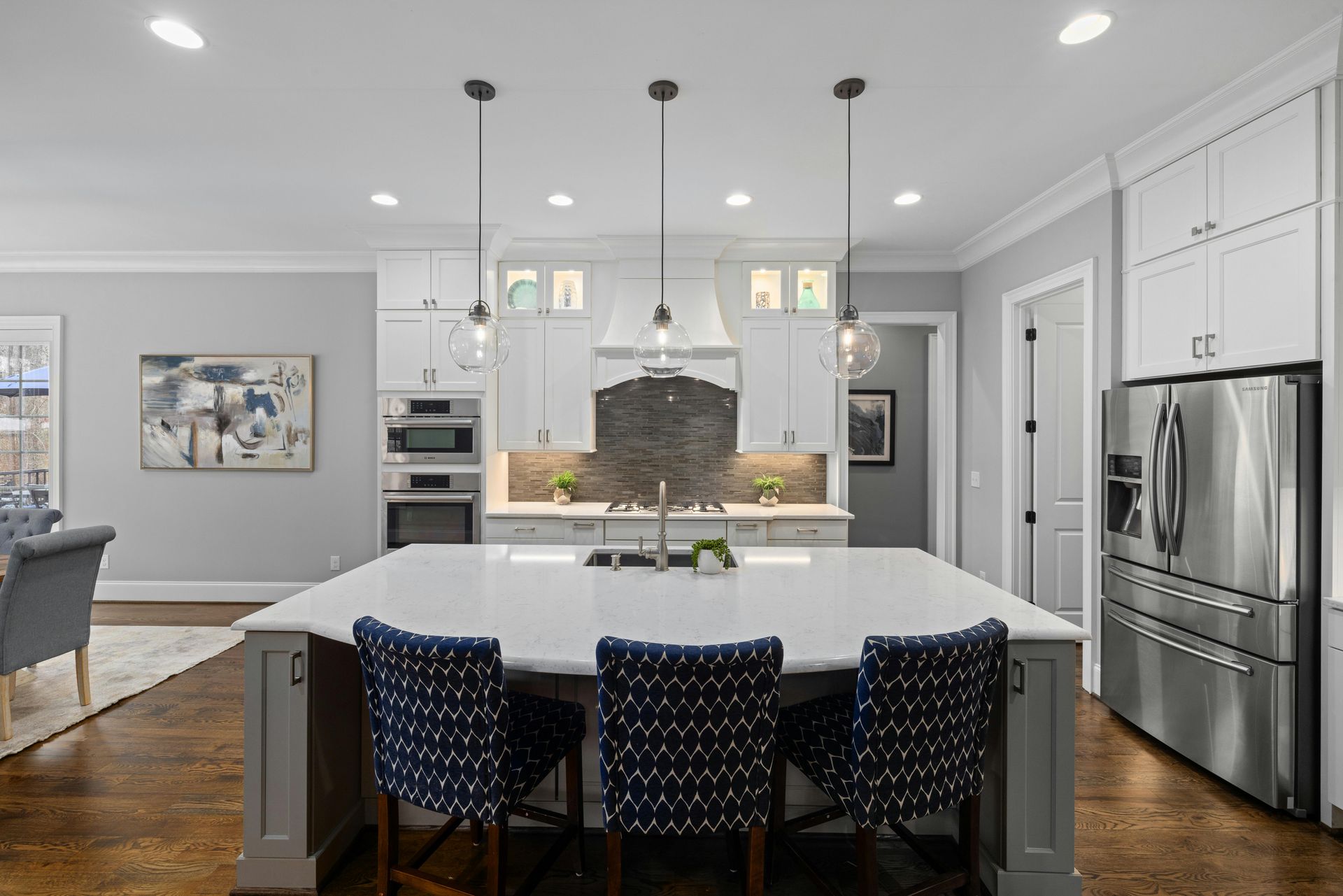 Modern kitchen with white cabinets, stainless fridge, large island, and three blue patterned stools