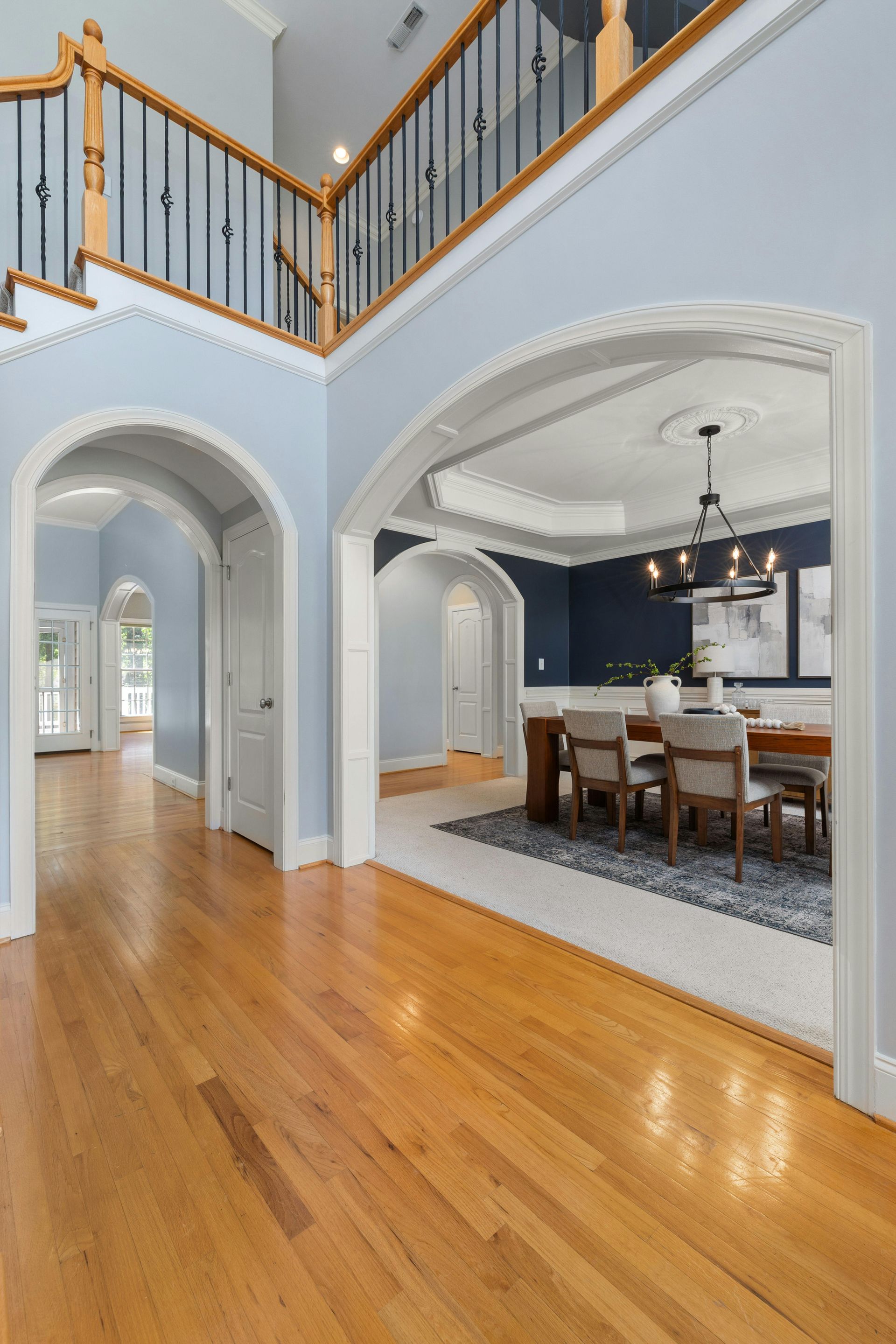 Bright foyer with hardwood floors, arched doorways, staircase, and a dining room with dark accent wall
