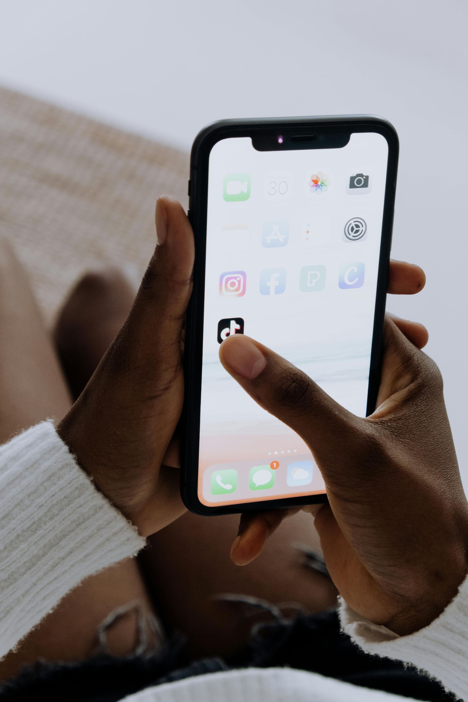 Hands holding a smartphone with app icons on the home screen.