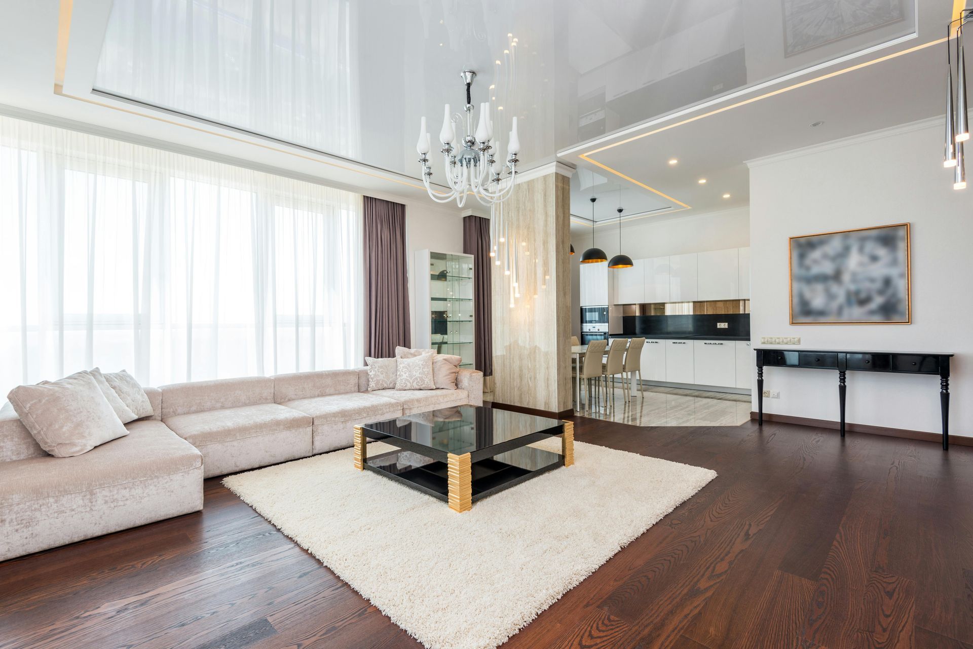 Modern open-concept living room with beige sectional, white rug, glass coffee table, and dark wood floors