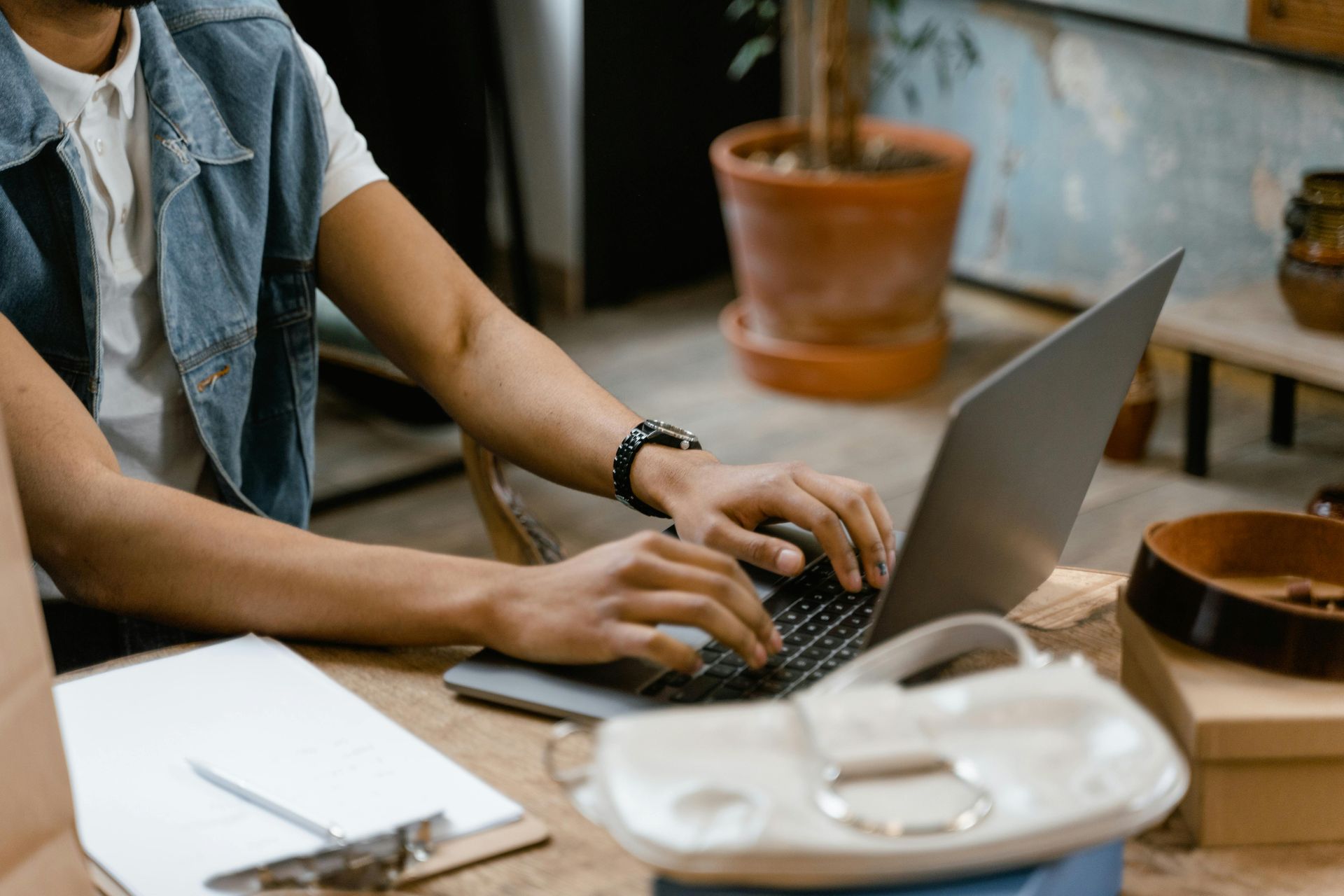 Person typing on a laptop at a wooden table with a notebook and cup in a cozy cafe setting