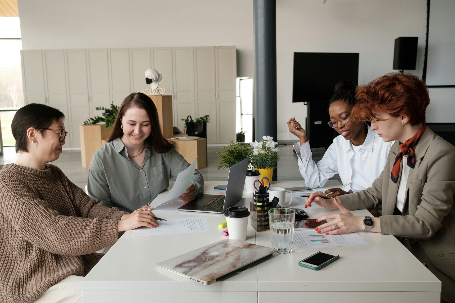 Four people meeting around a table, reviewing papers and laptops in a bright office conference room