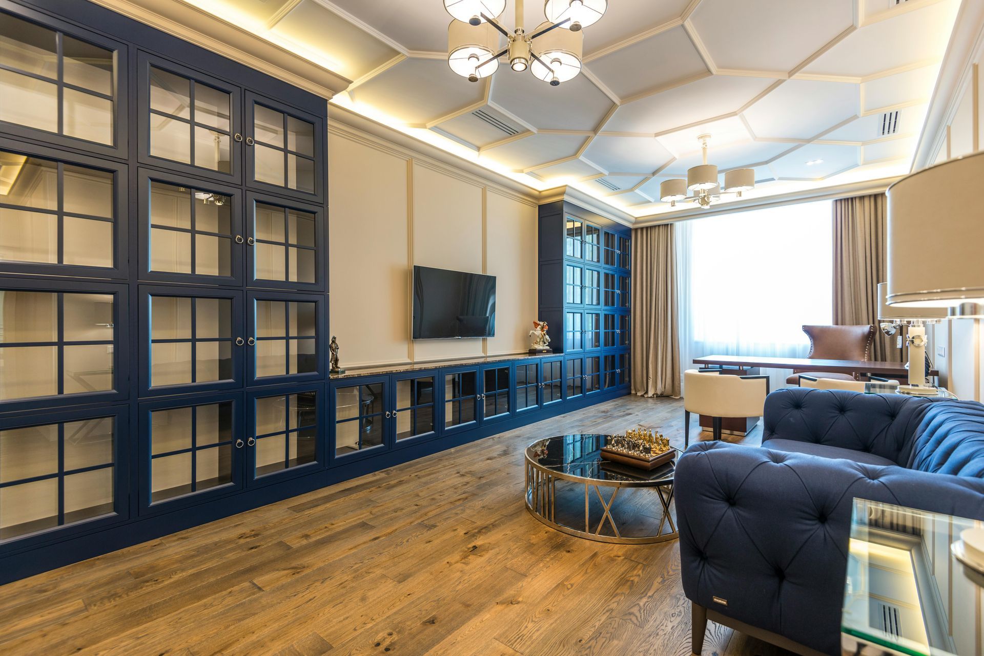 Elegant living room with navy built-ins, wall-mounted TV, tufted sofas, and wood floors under modern lighting