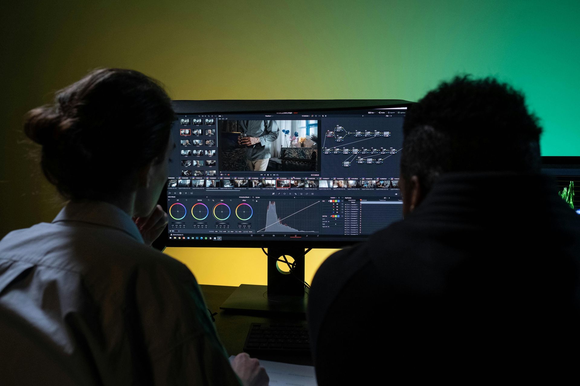 Two people reviewing video editing on a dual-monitor workstation in a dark room