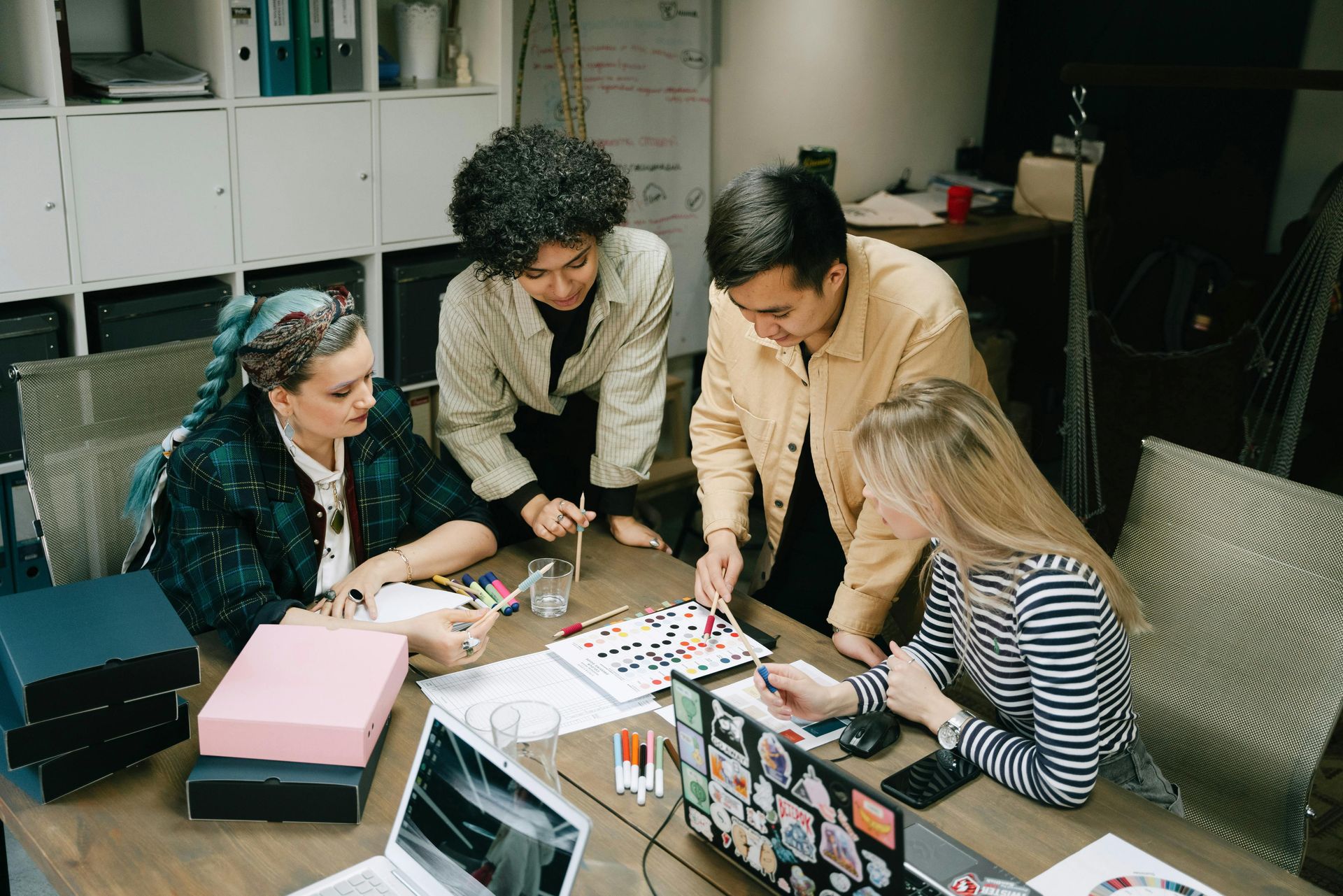 Four people collaborating around a desk with papers and supplies in a bright office