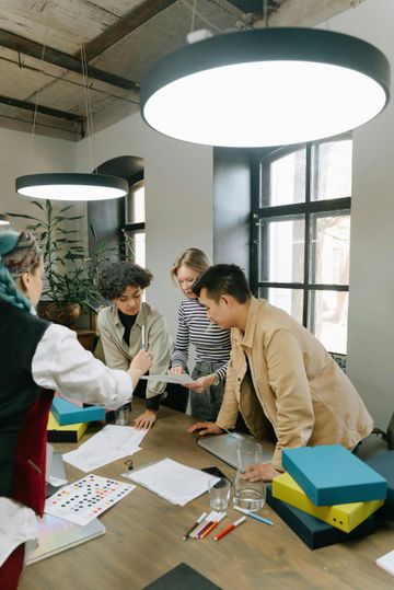 People collaborating around a table in a bright office, reviewing papers and design samples.