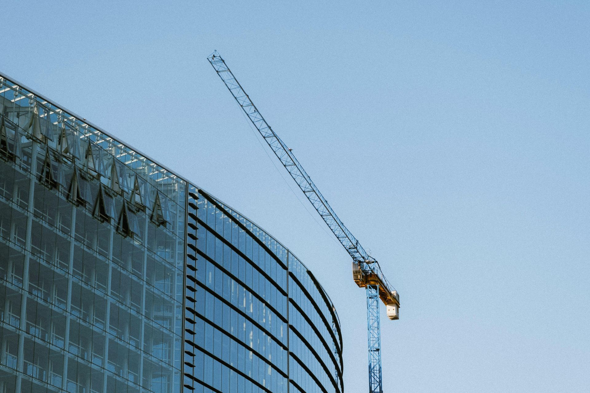 Construction crane beside a curved glass building under a clear blue sky