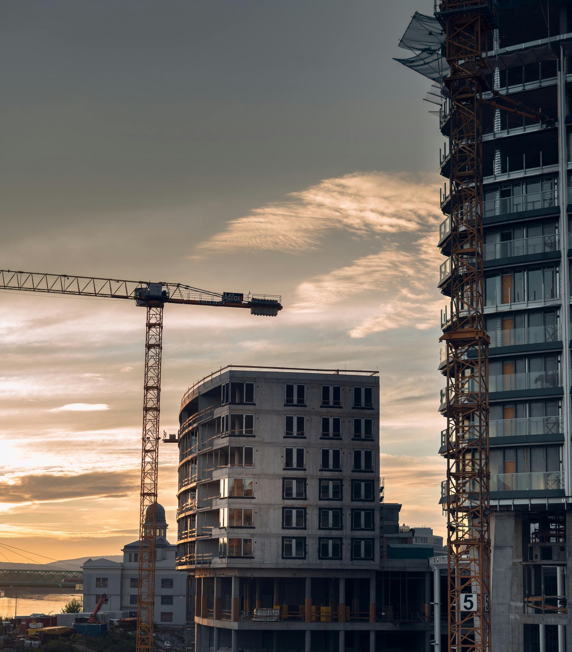 Crane and high-rise buildings under construction at sunset, with a cloudy sky.