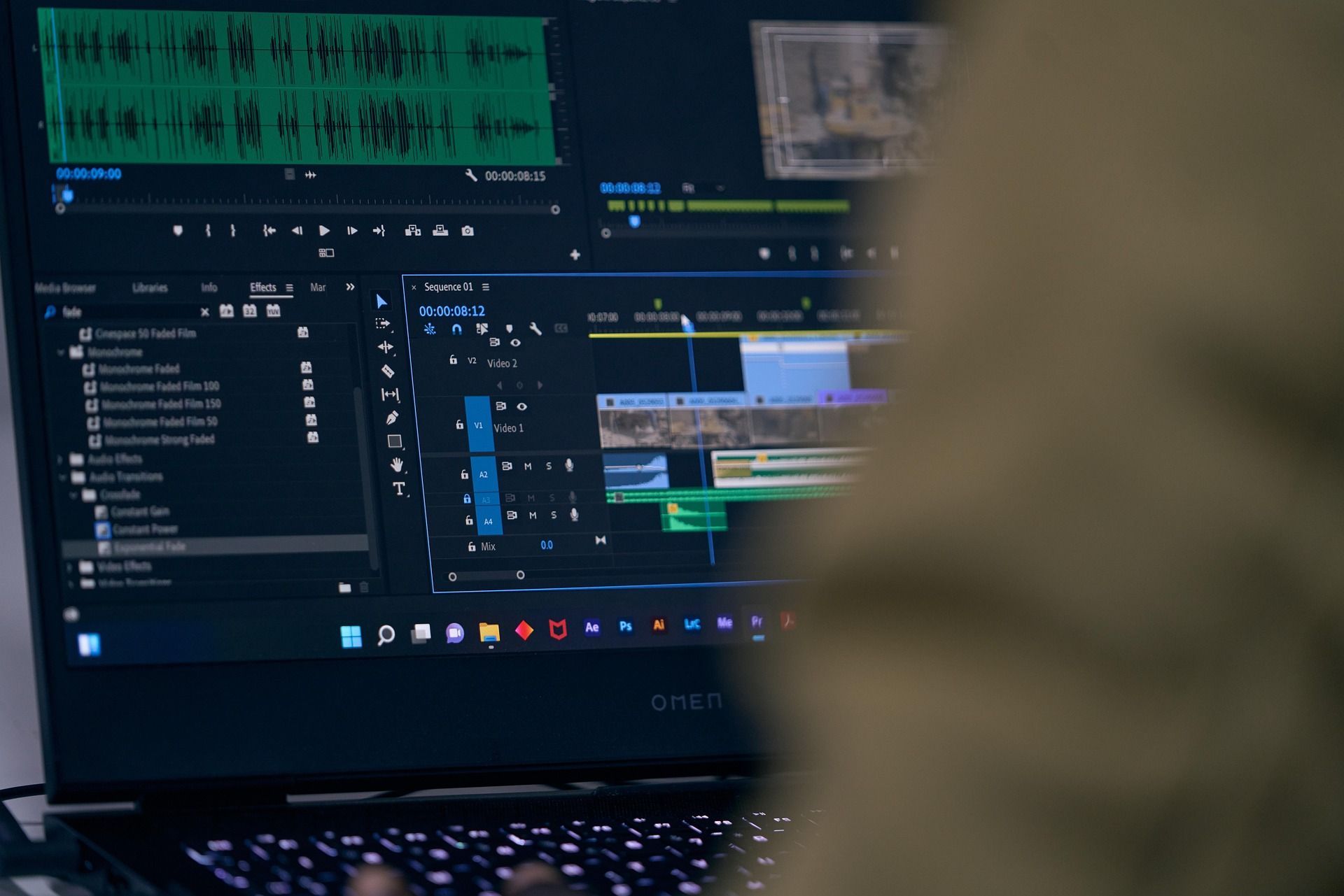 Laptop screen showing video editing software with audio waveforms and a timeline being edited