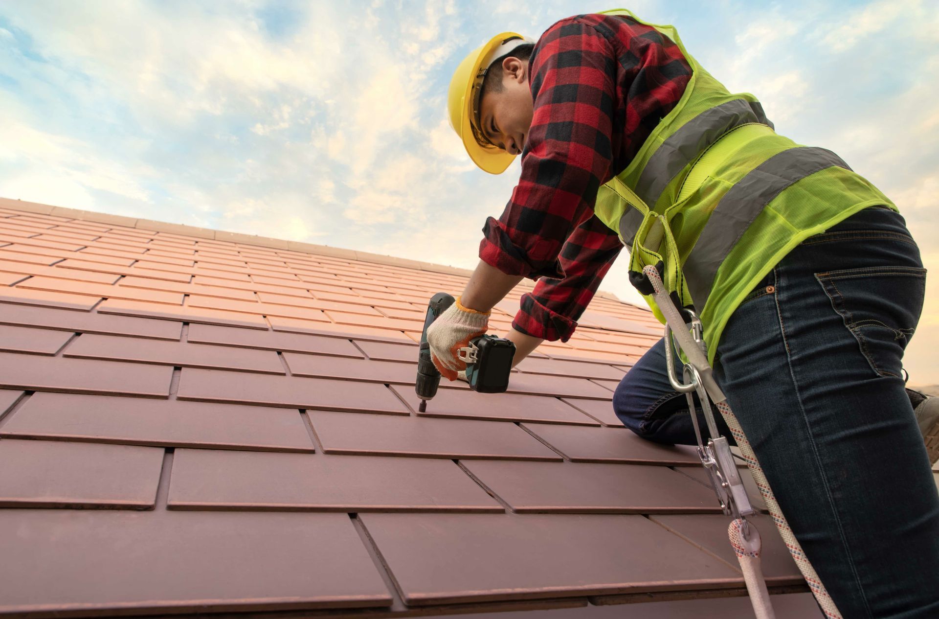 Roofer wearing work wear gloves, using a nail gun, installing a concrete roofing tile.