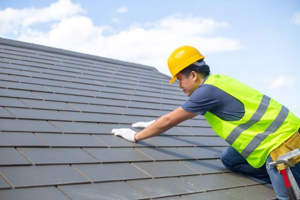 Roofing contractor installing dark shingles on residential roof wearing safety helmet.