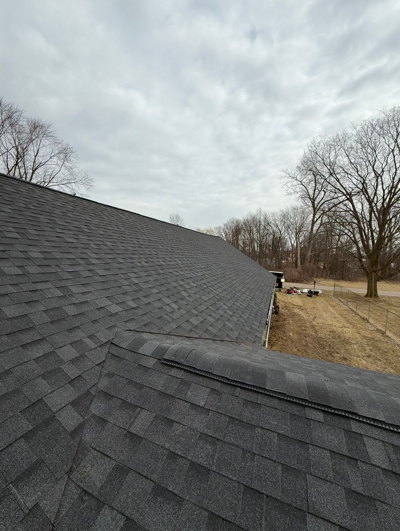 Dark gray shingle roof under cloudy sky; trees and grass in background.