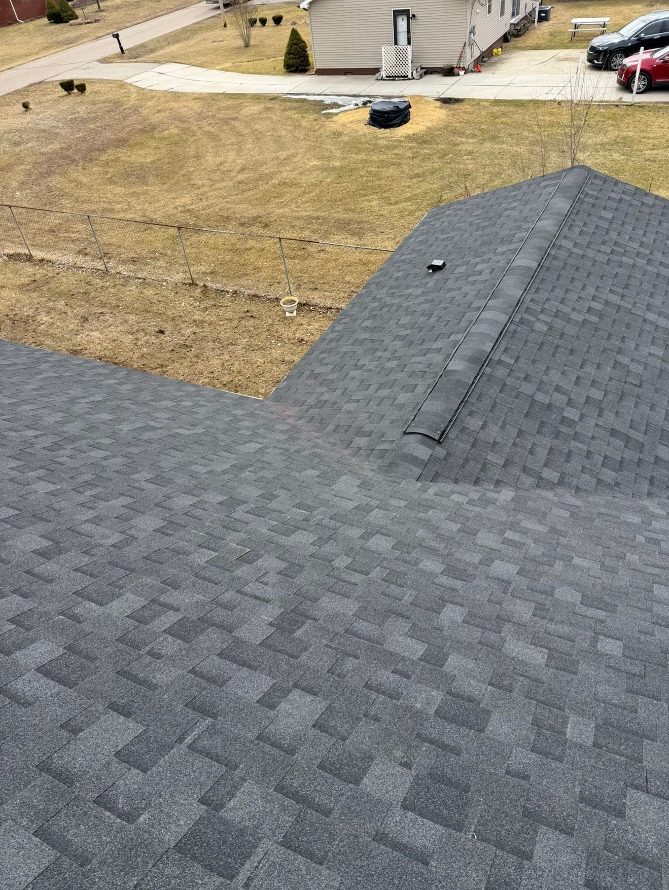 Dark gray shingle roof of a house with a surrounding dry, grassy landscape.
