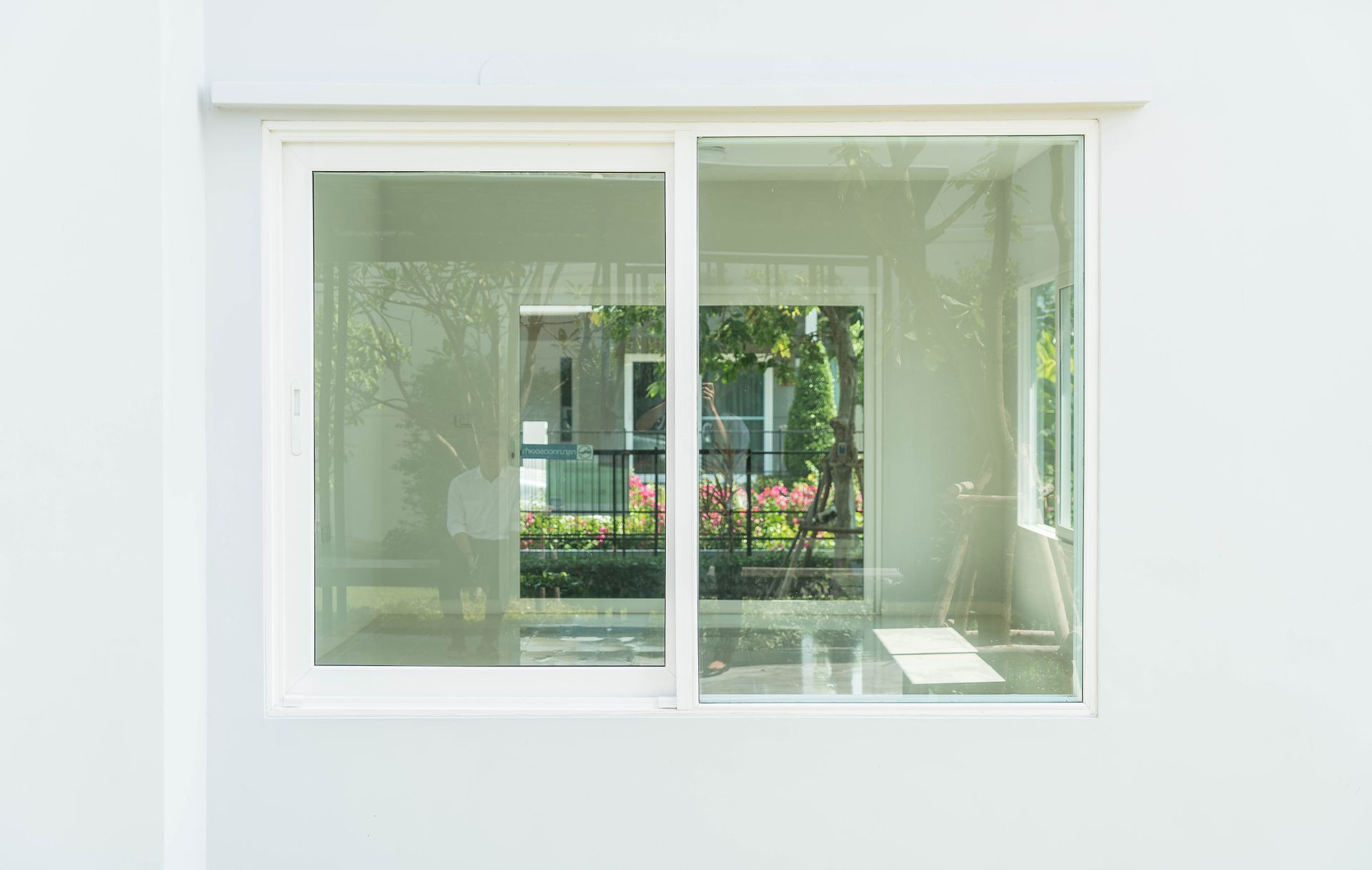 White sliding glass window on a white wall, reflecting a yard and building — Fast Glass & Glazing In Manilla, NSW