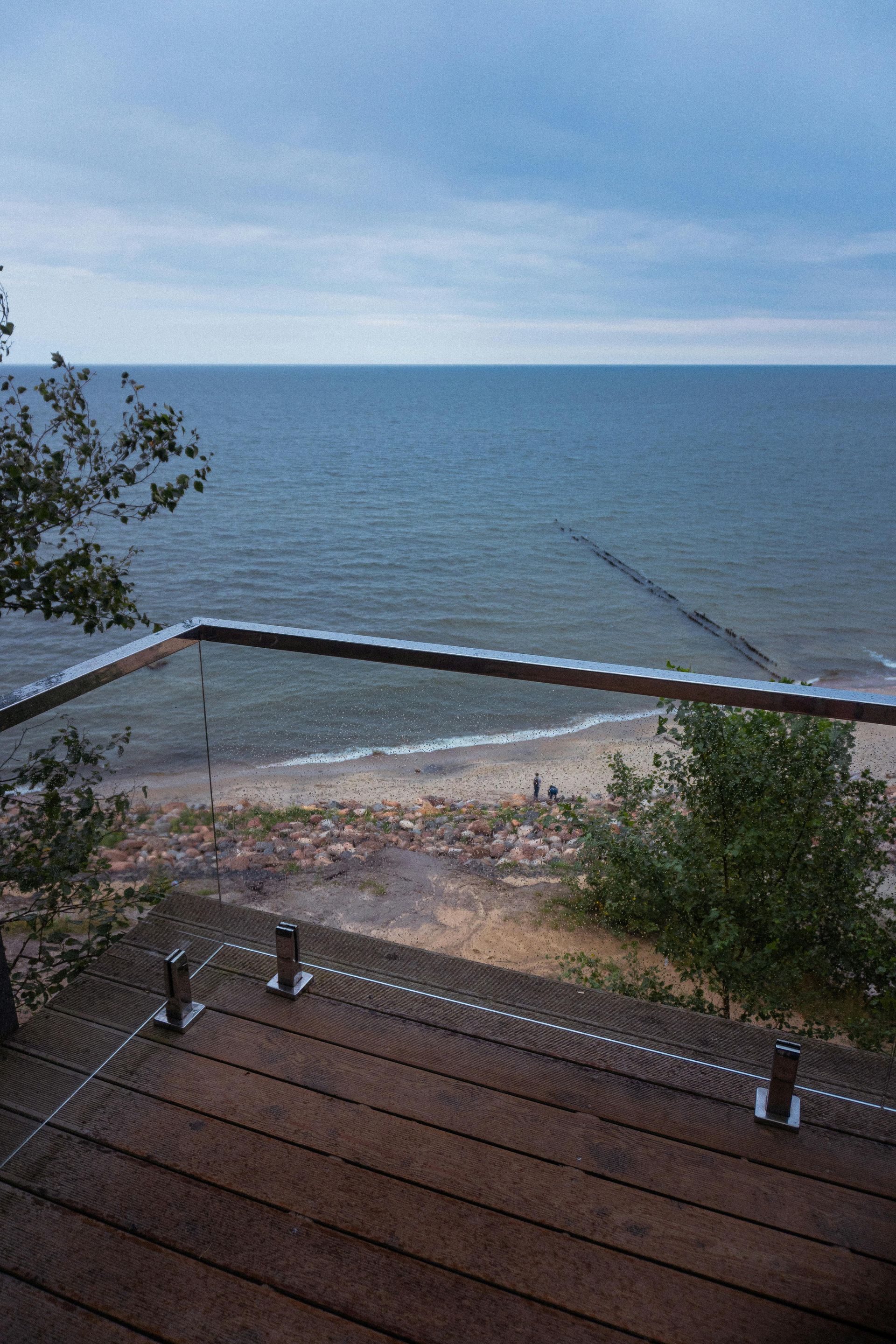 Wooden deck with glass railing overlooking a beach and ocean under a cloudy sky — Fast Glass & Glazing In Barraba, NSW
