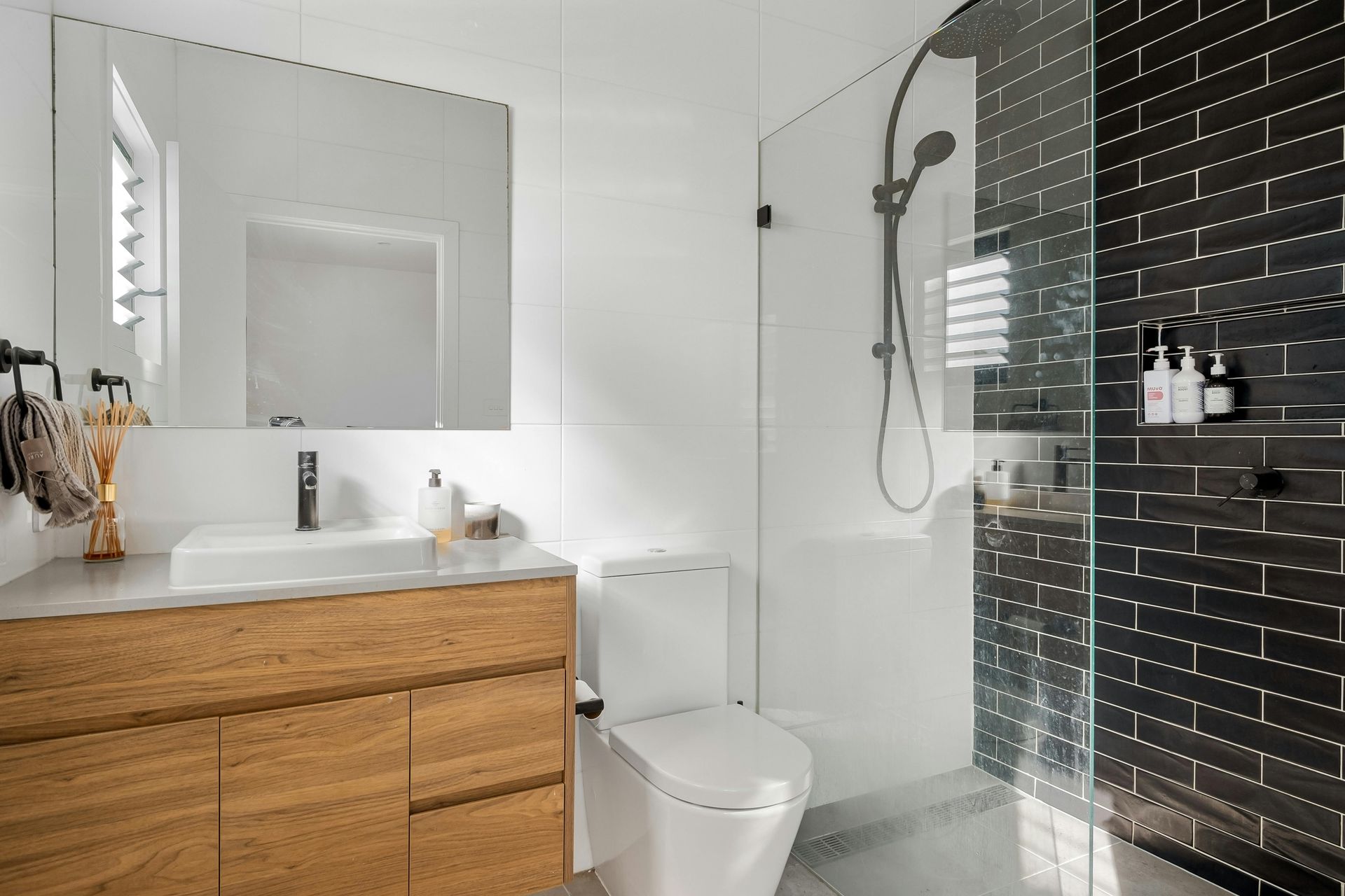 Modern bathroom with wooden vanity, white toilet, black tiled shower, and glass door — Fast Glass & Glazing In Tamworth, NSW