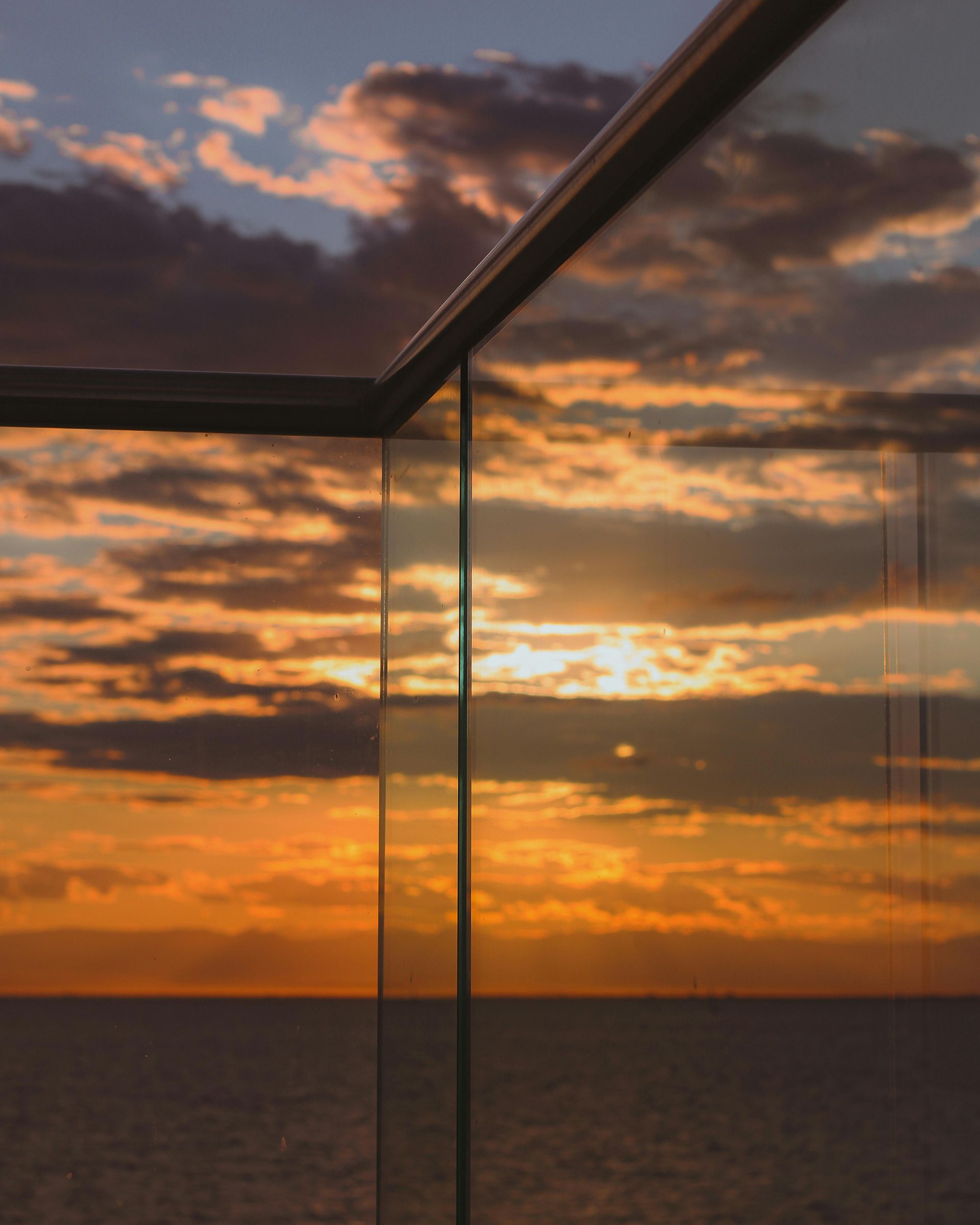 Sunset over the ocean, framed by glass panels and a railing — Fast Glass & Glazing In Manilla, NSW