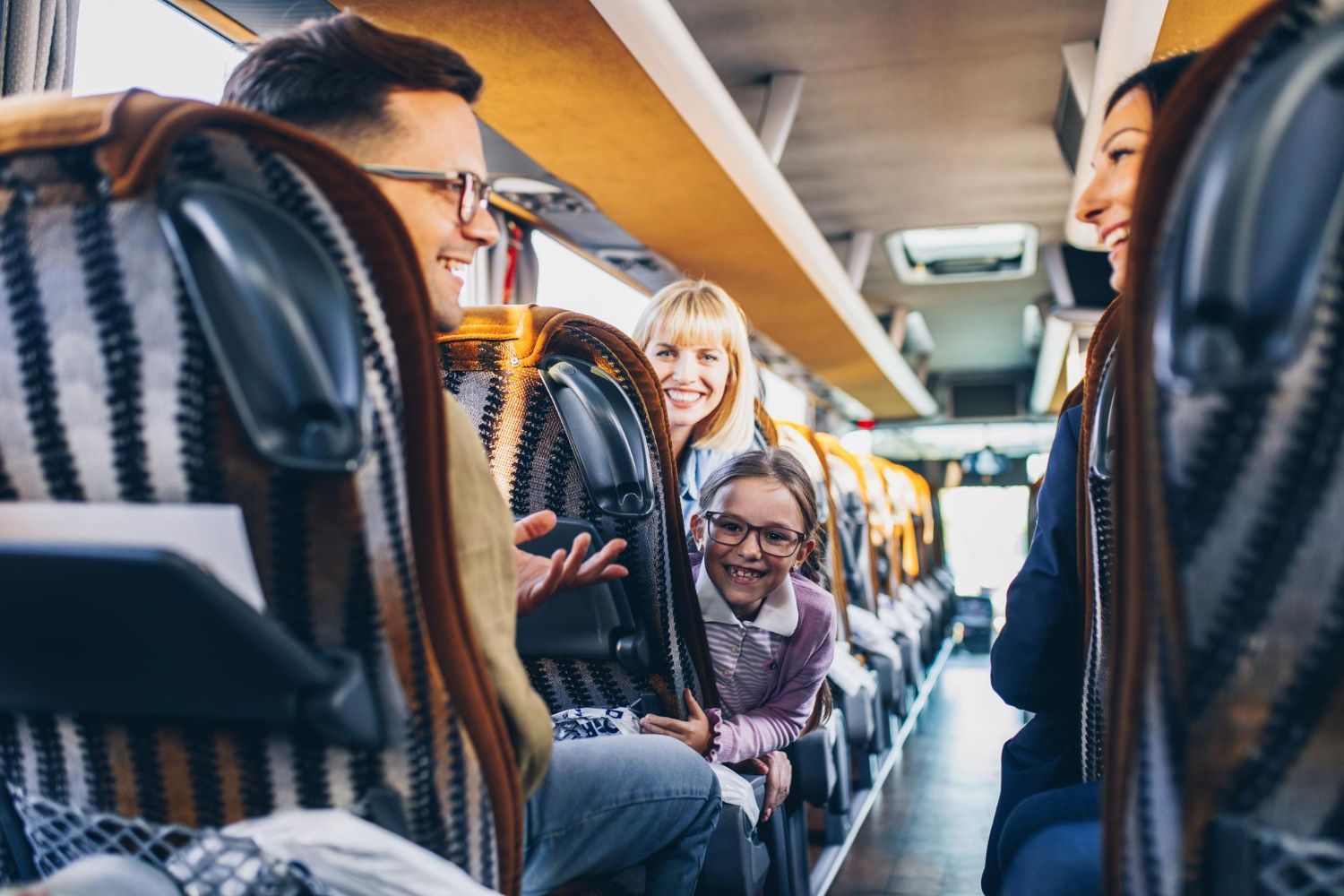 A family smiling and talking together while seated in the rows of a bus.