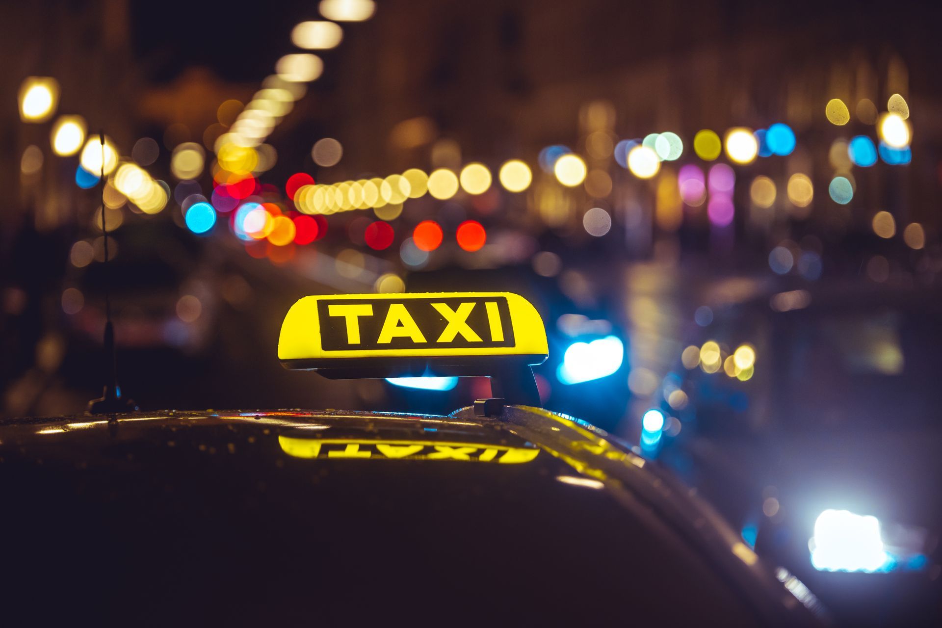 Yellow taxi sign glowing on a car at night with blurred city lights in the background
