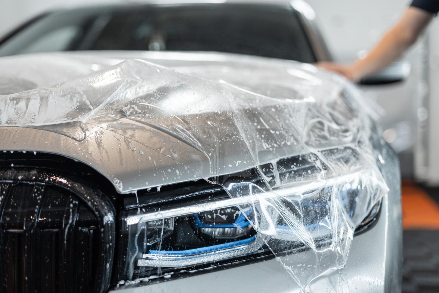 A clear protective film is being applied to the hood and headlight of a silver car with soapy water.