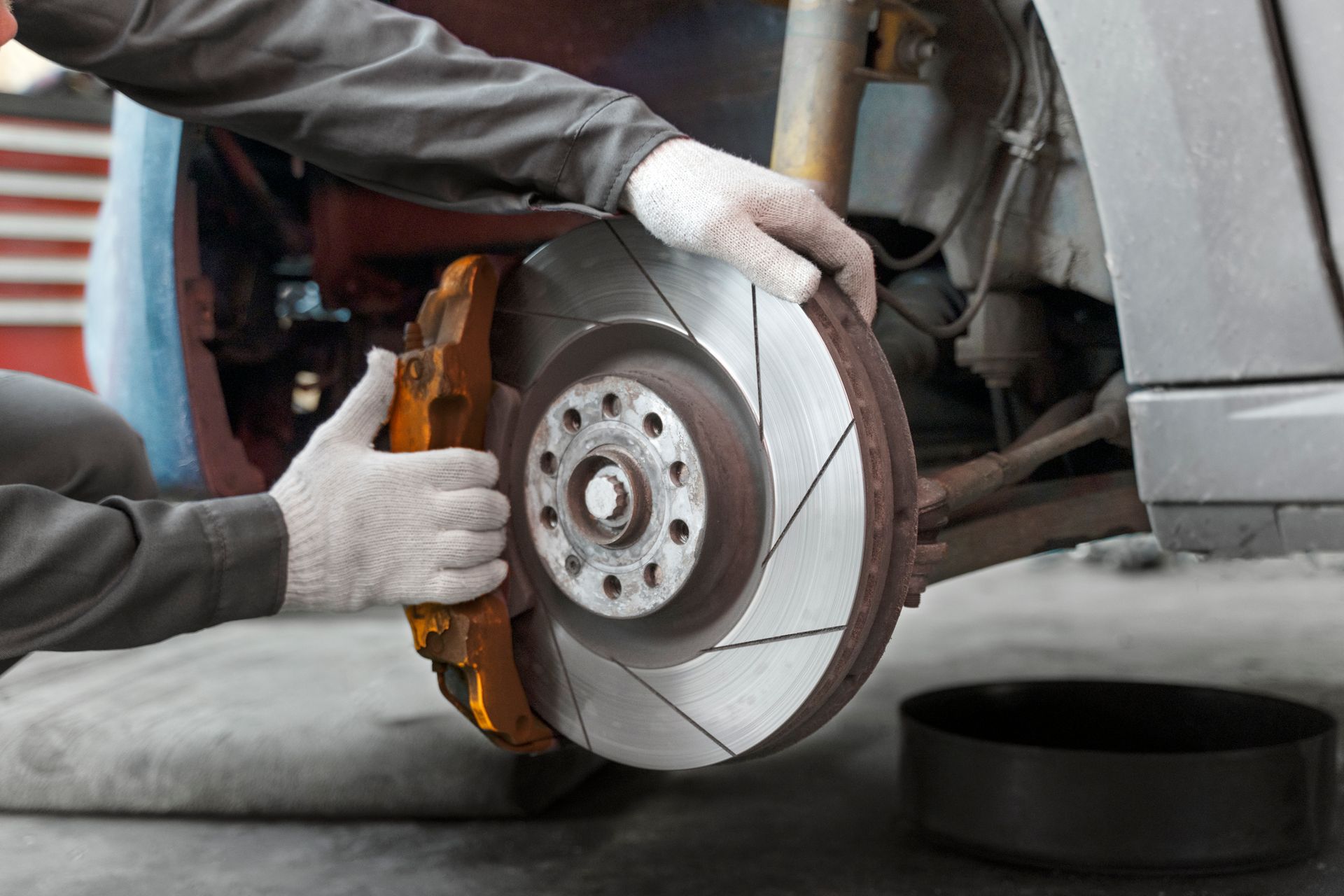 Mechanic replacing a car brake rotor and caliper with gloved hands