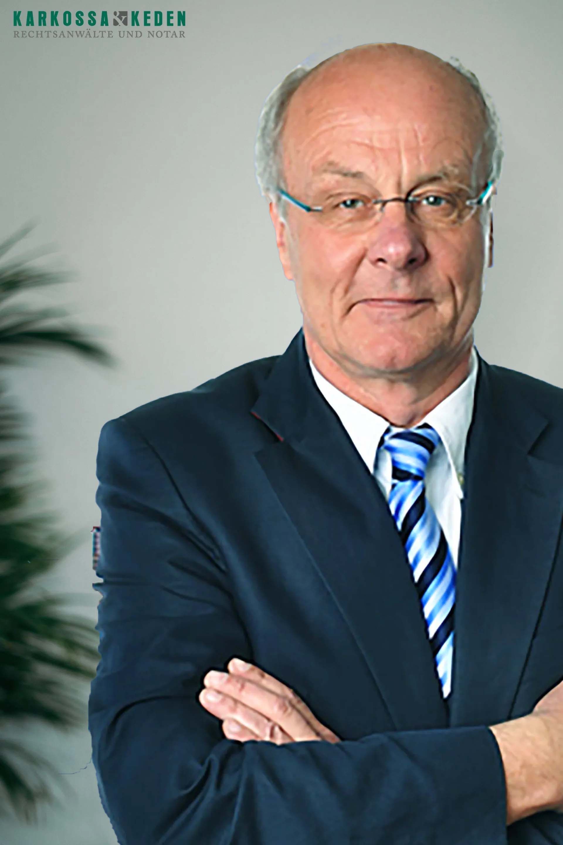 Mann im Anzug mit verschränkten Armen und Brille, der den Betrachter ansieht.