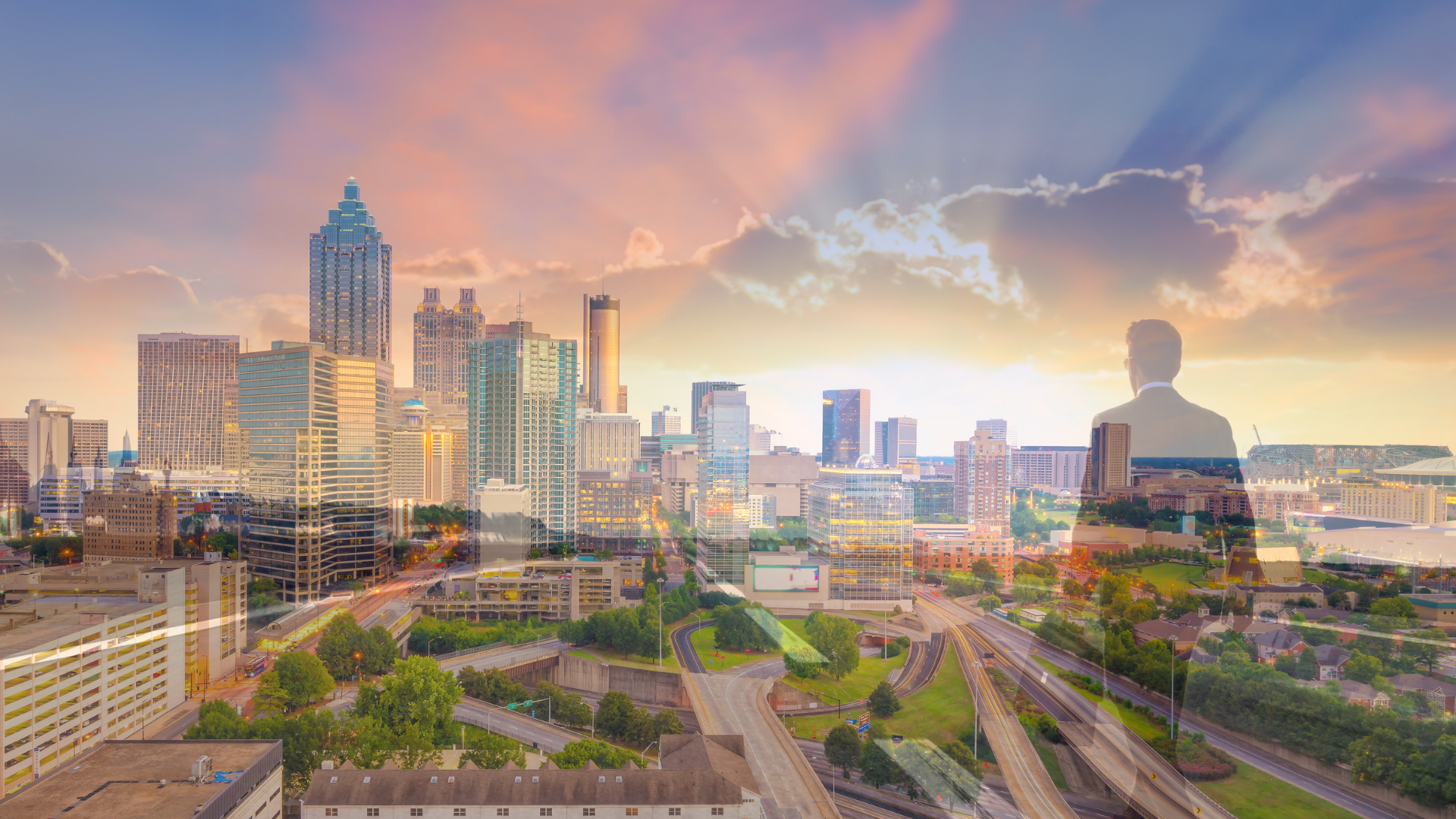 A man is standing in front of a city skyline at sunset.