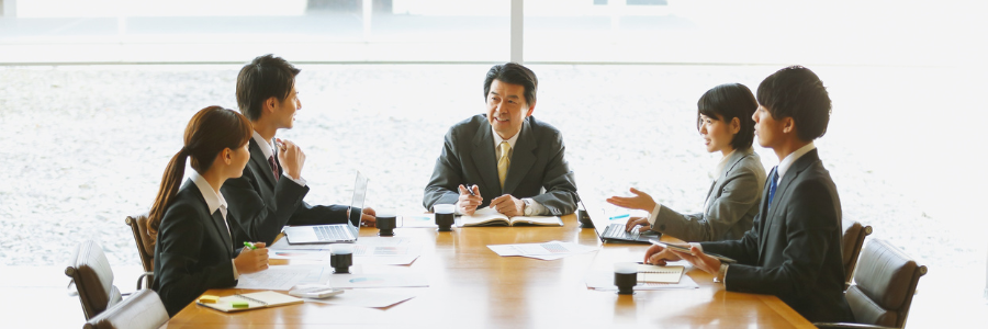 A group of people are sitting at a table writing on a clipboard.