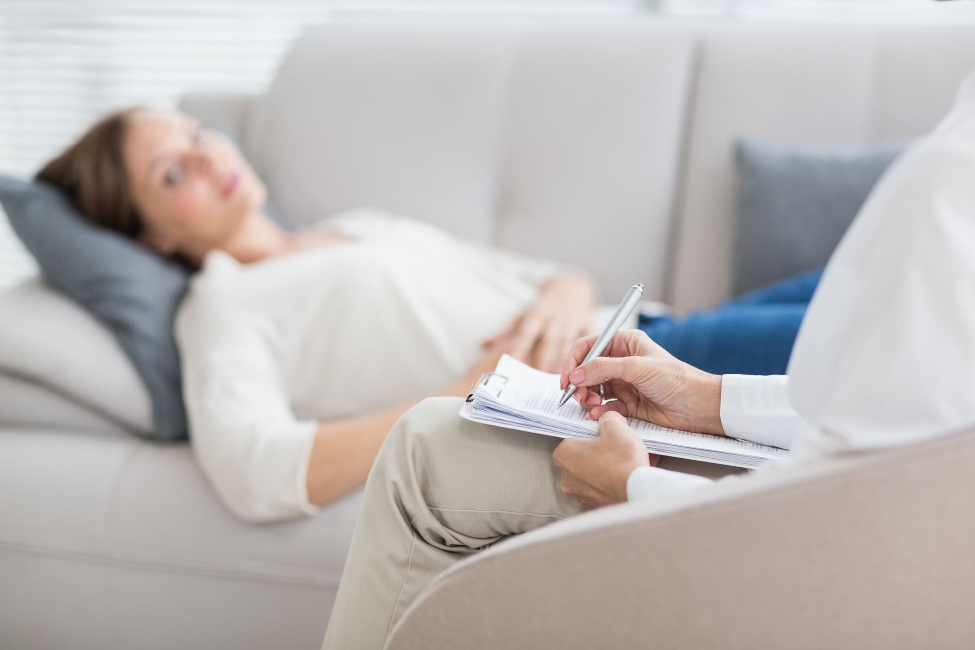 Therapist taking notes while a client lies on a couch in a bright counseling room