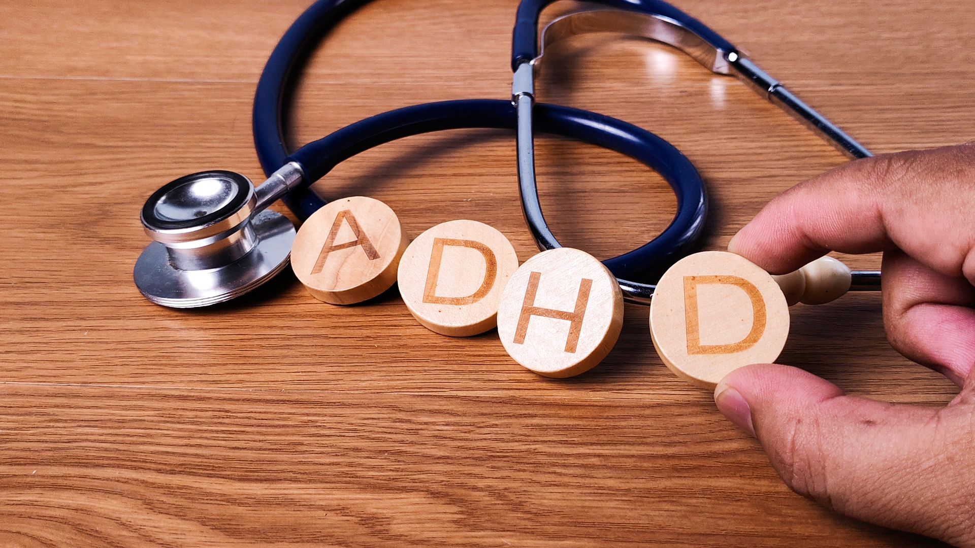 Stethoscope and wooden letters spelling ADHD on a desk, held by hands. Stethoscope and wooden letters spelling ADHD on a desk, held by hands.