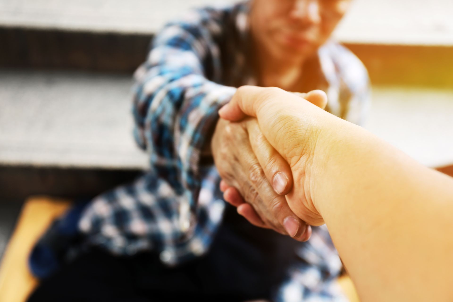Hand clasp in foreground, with a person sitting on a couch in the blurred background