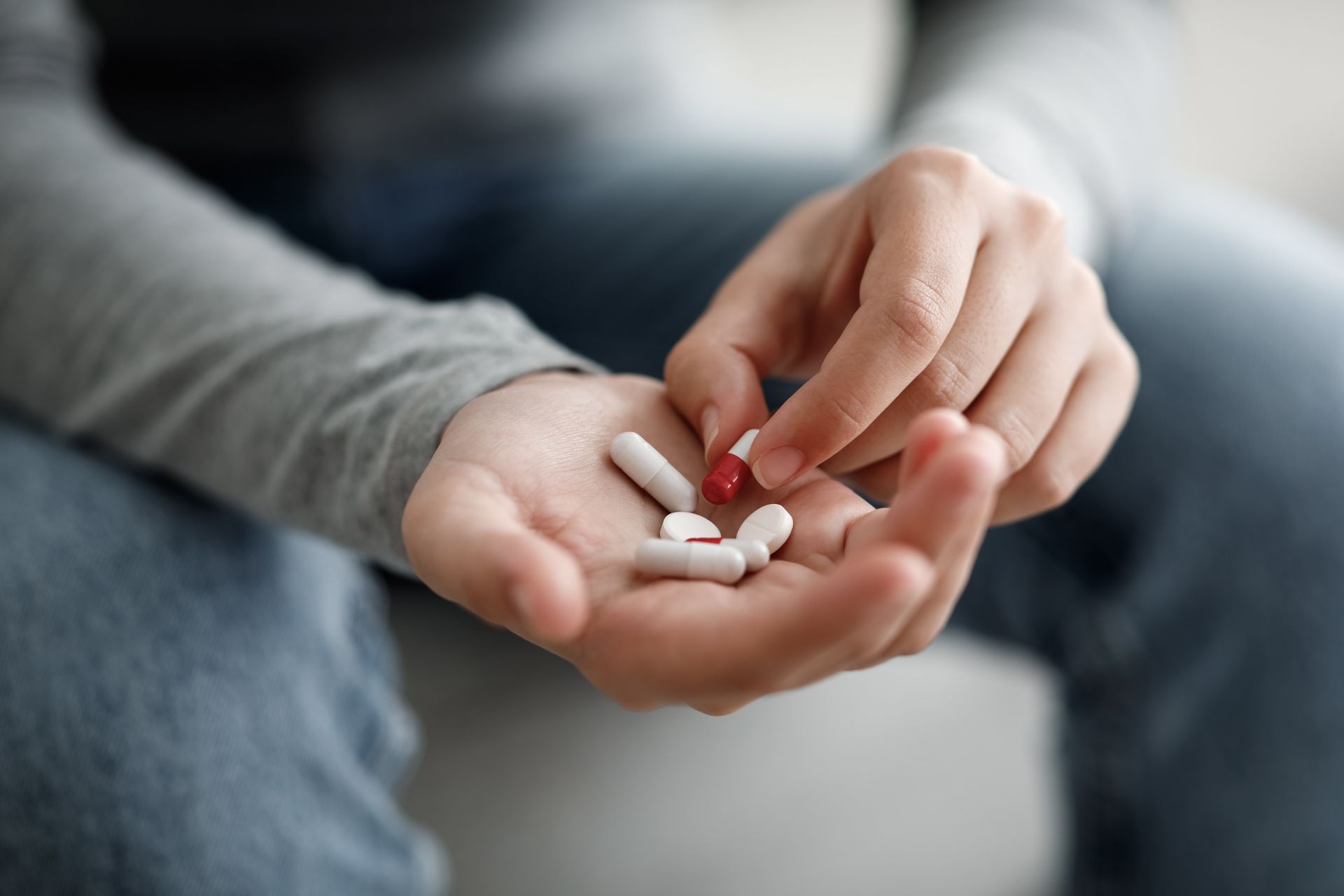 Hands holding small white and red pills over a blurred couch. Hands holding small white and red pills over a blurred couch.
