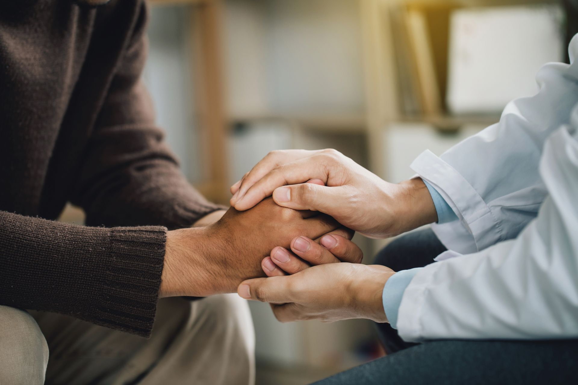 Two people holding hands in a supportive gesture indoors