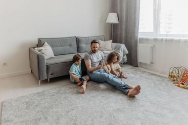 Person vacuuming a light beige rug in a bright living room with a hose and canister vacuum