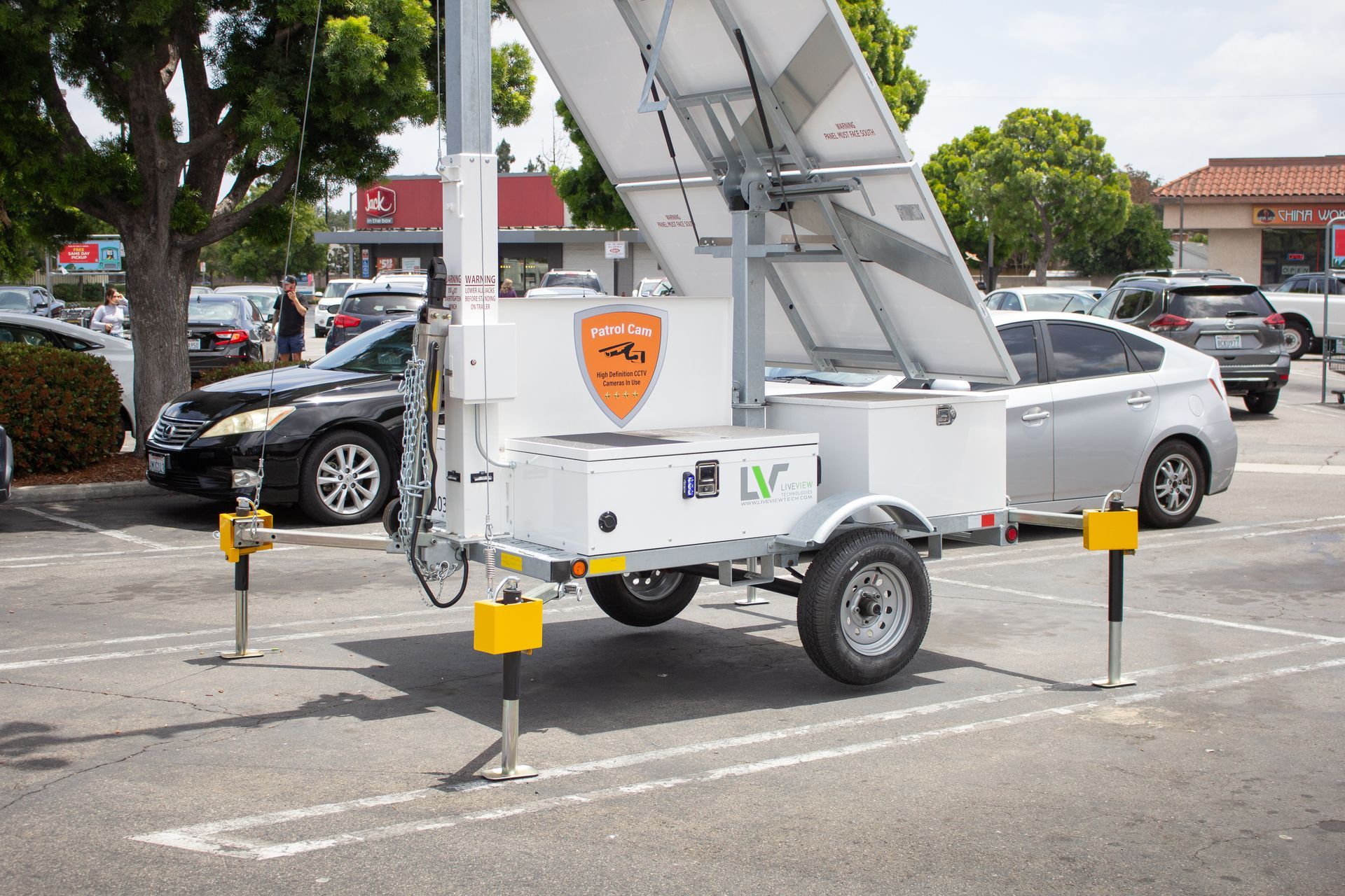 Solar-powered mobile unit in a parking lot with raised solar panels. Black car behind.