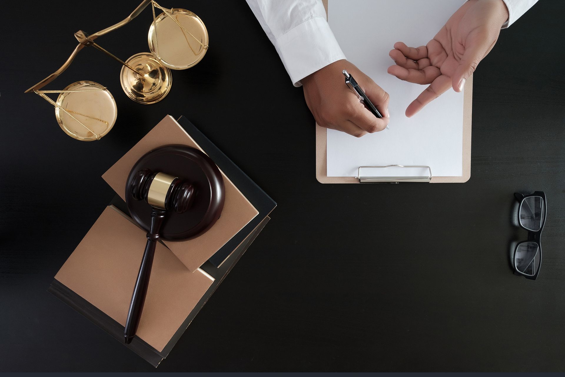 Criminal law attorney writing on clipboard with gavel, legal scales, and books on desk. 