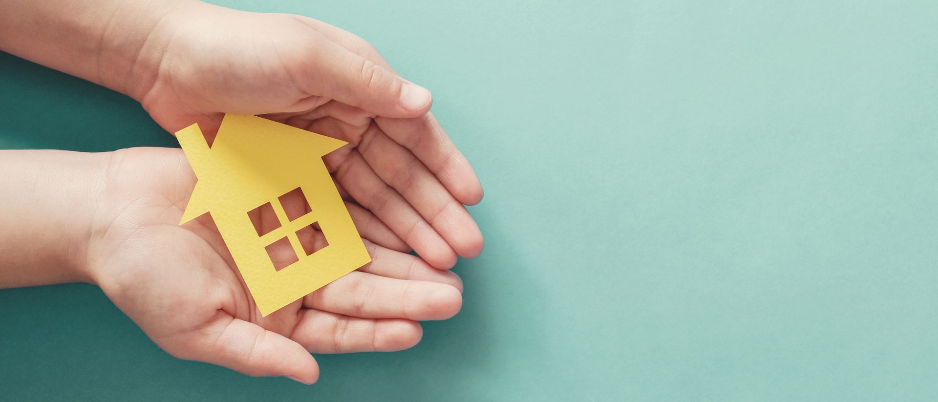 Hands holding a small yellow house icon on a teal background