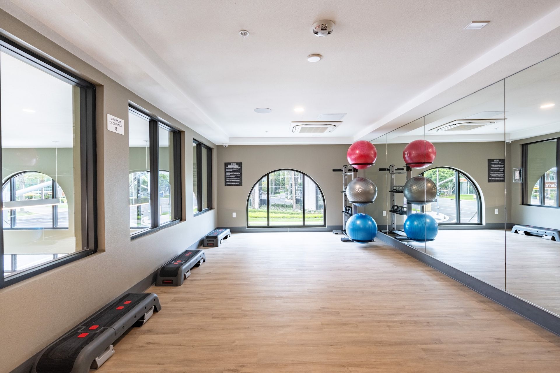 Gym with exercise balls, step platforms, large windows, and a mirrored wall.