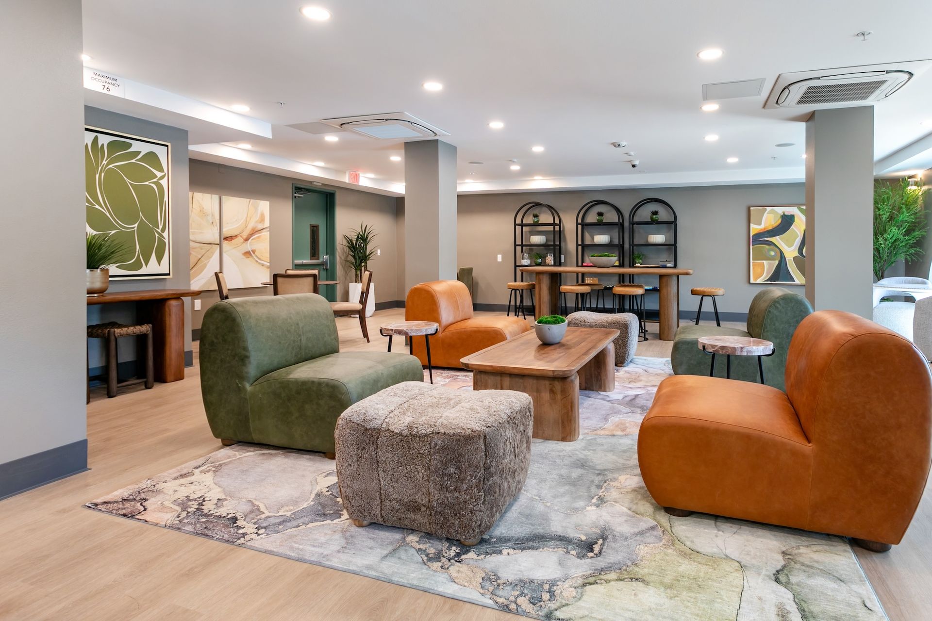 Modern lounge with orange and green chairs, wood tables, and abstract art.