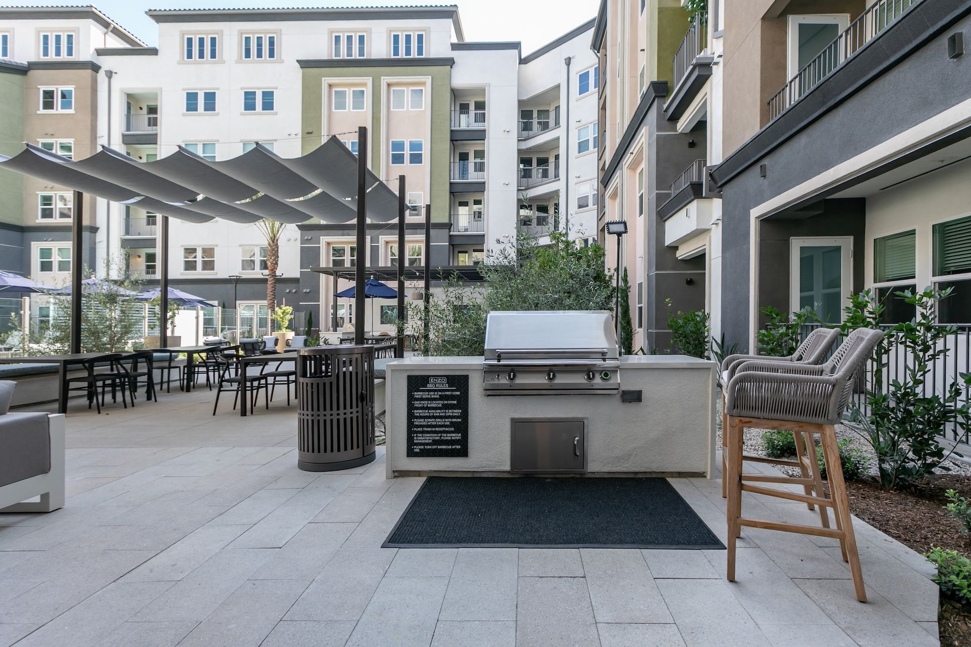 Outdoor patio with a grill, seating, and multi-story apartments.