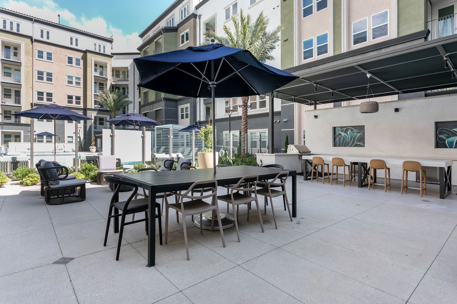 Outdoor patio with tables, chairs, and umbrellas, adjacent to apartment buildings.