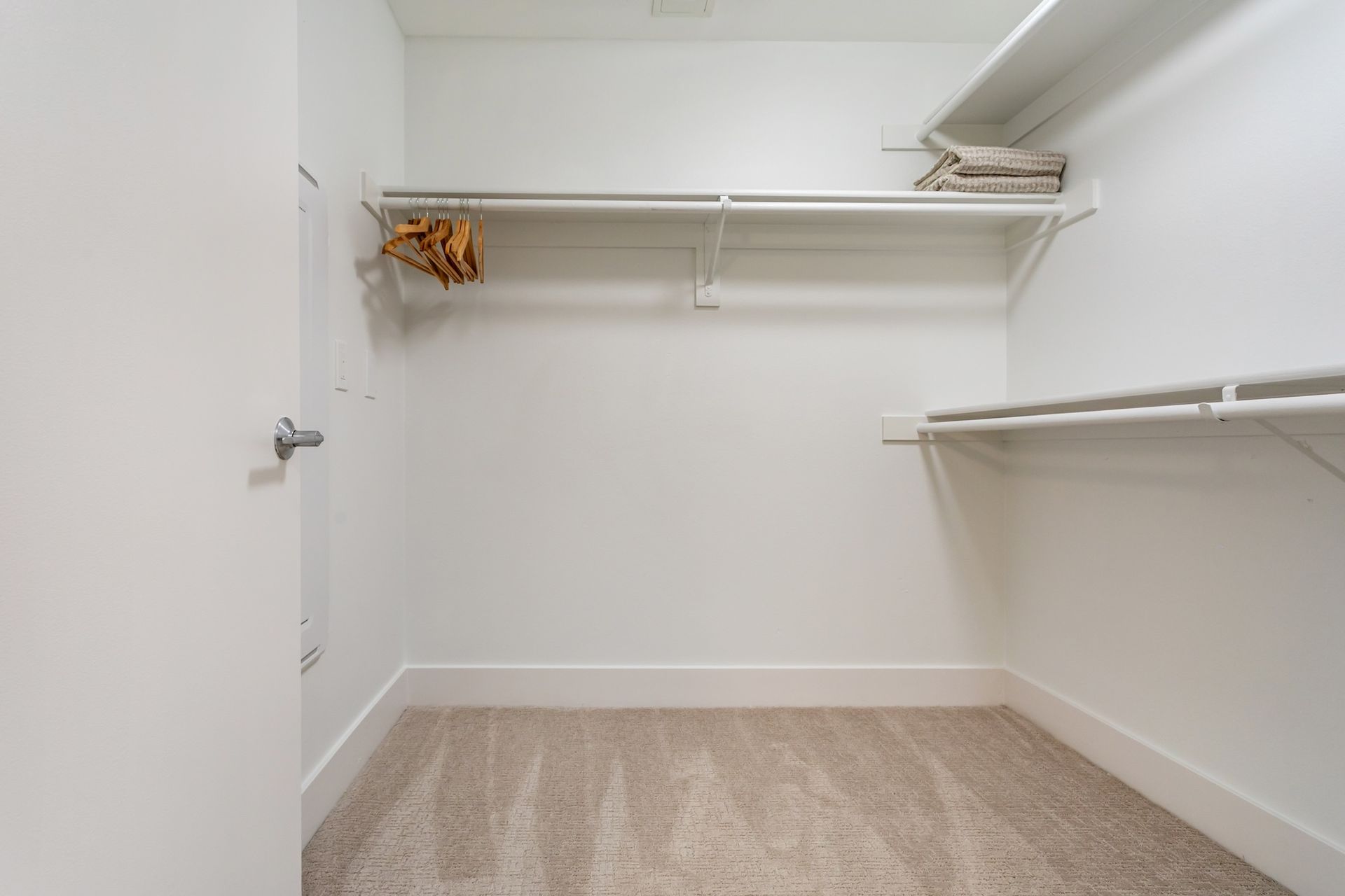 Empty walk-in closet with beige carpet, white shelves, and a few wooden hangers.
