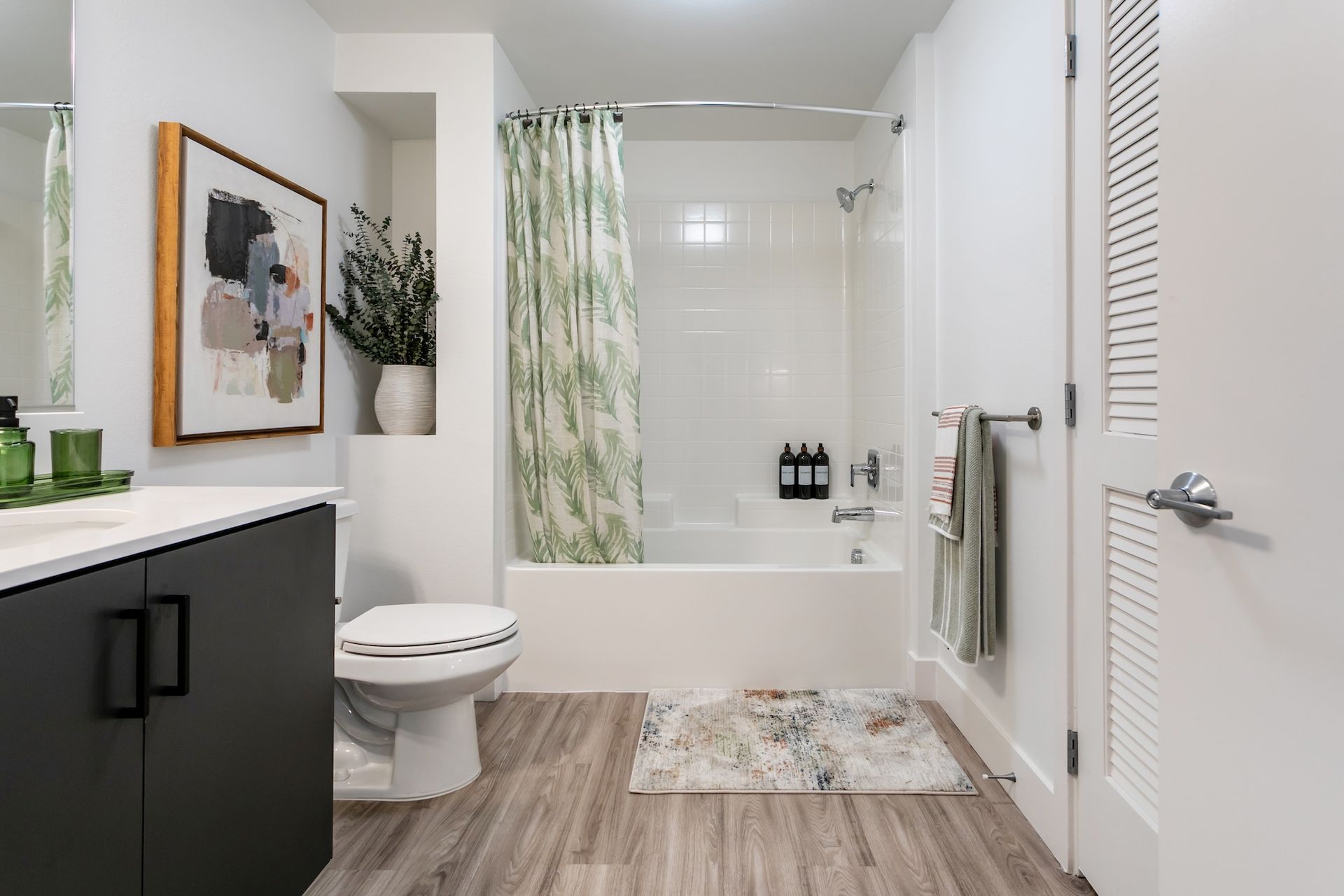 Modern bathroom with white tub, green shower curtain, dark vanity, and wooden floor.