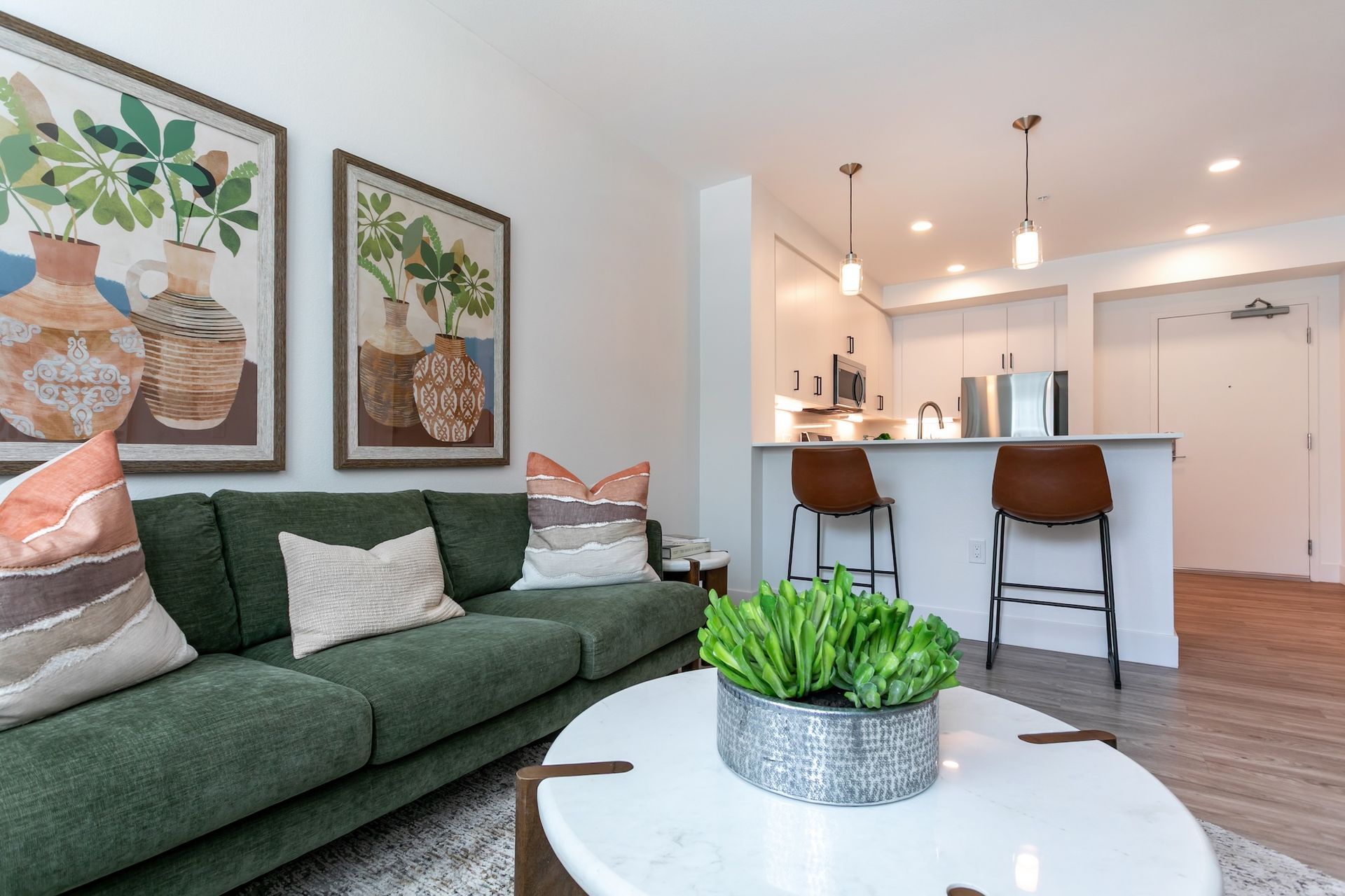 Green couch in modern living room with art, open kitchen, and bar stools.